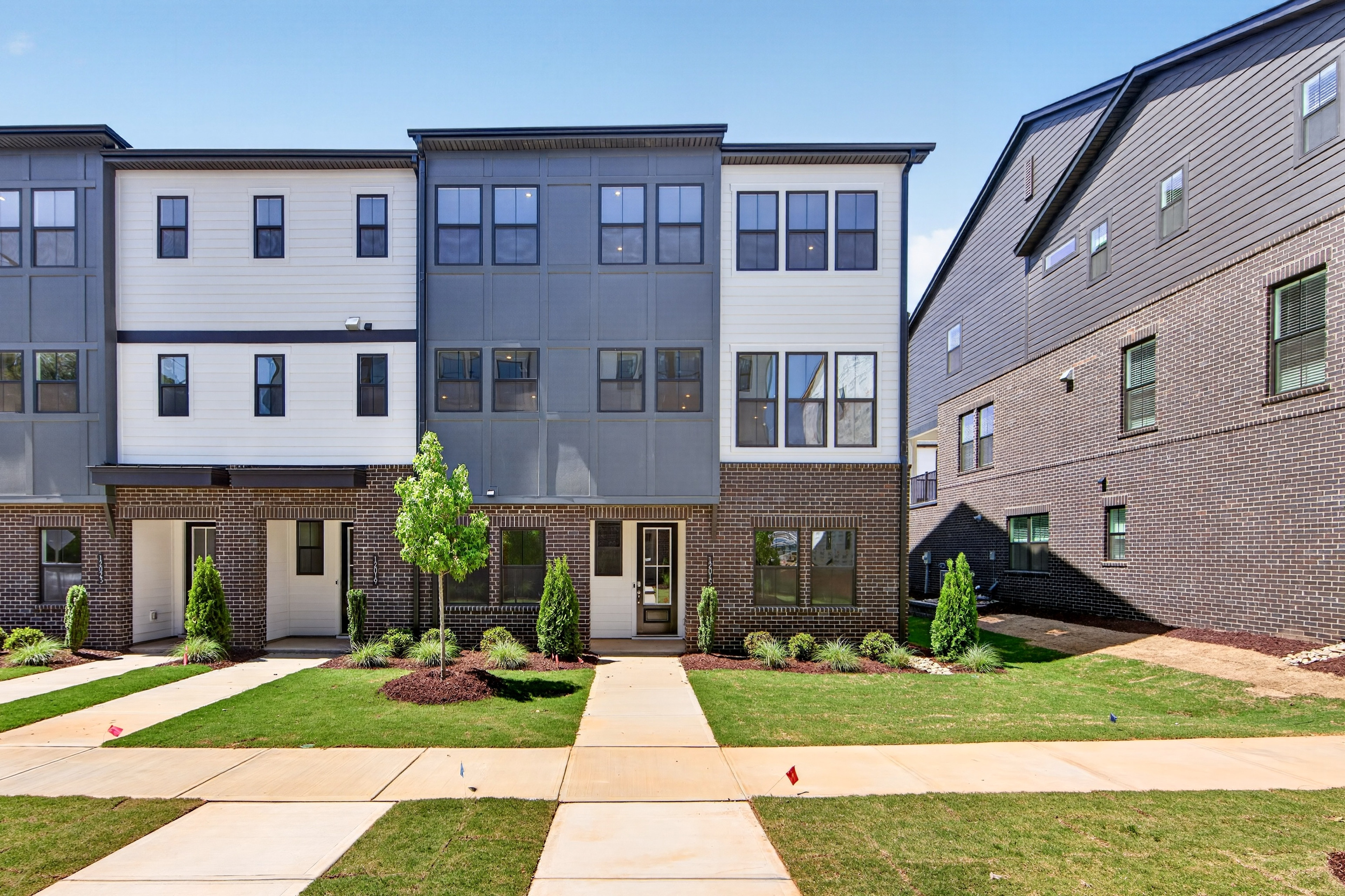 A row of modern townhouses with well-manicured lawns and landscaping, set against a backdrop of other residential buildings.