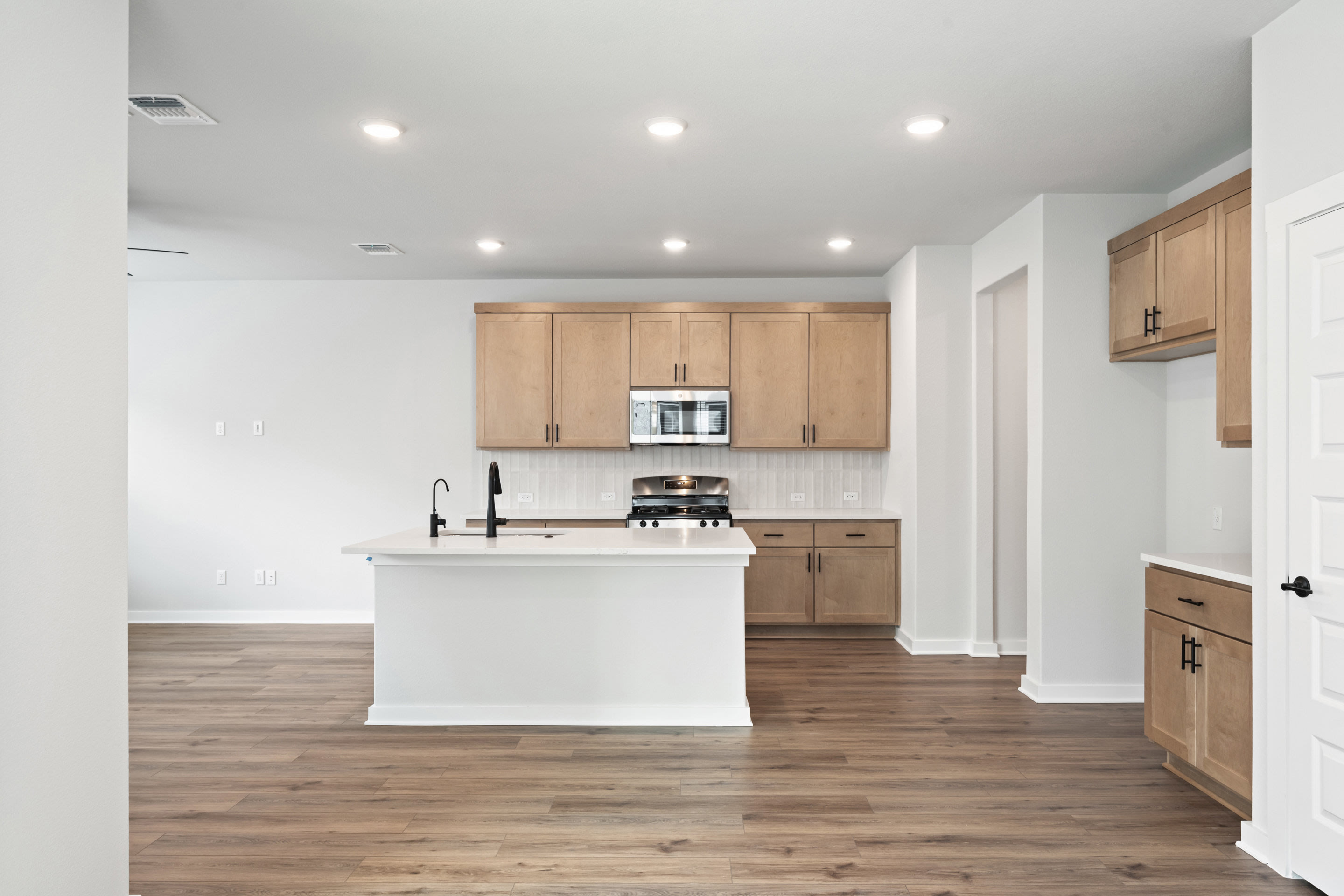 A modern kitchen with a white island in the foreground and light wood cabinets and appliances in the background.