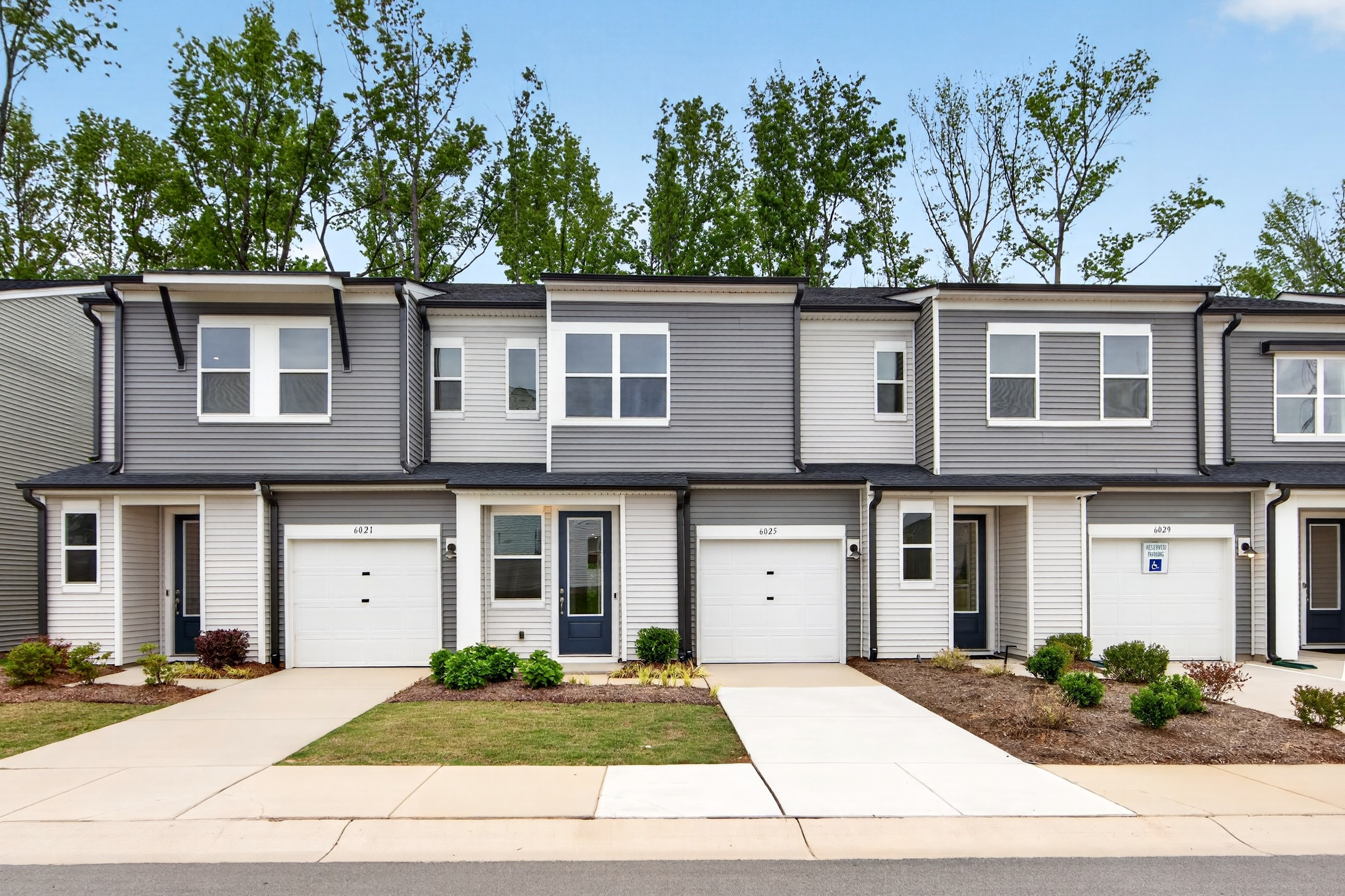 Modern townhouses with manicured lawns in the foreground are set against a backdrop of lush green trees.