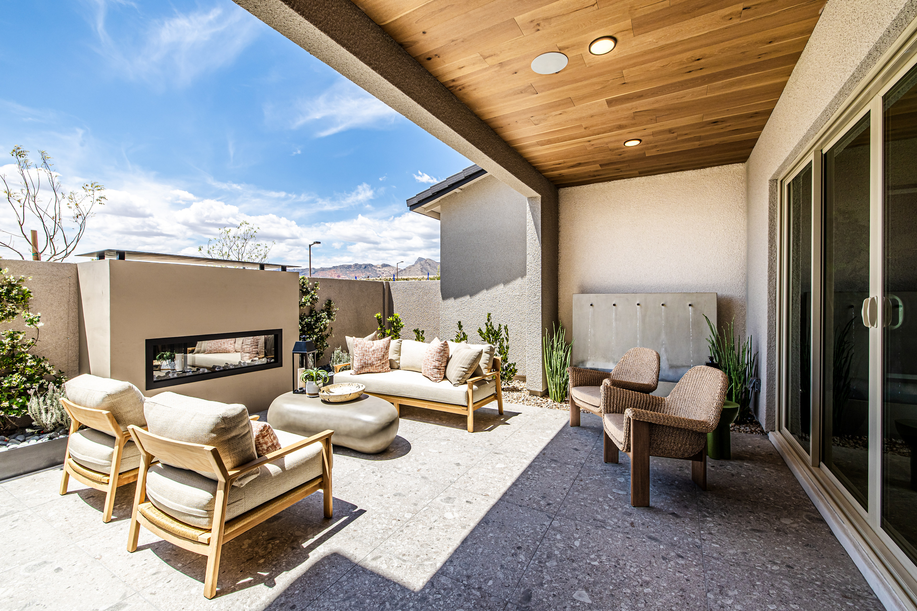 A modern patio with comfortable seating and a fireplace is set against a backdrop of a bright blue sky and distant hills.