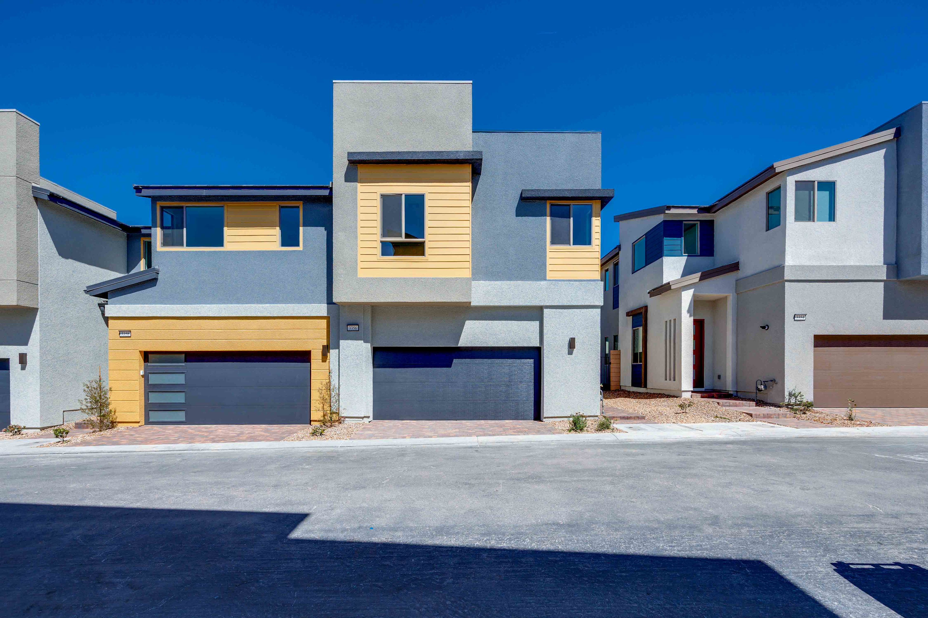 Modern townhouses with gray and yellow exteriors stand in front of a clear blue sky.