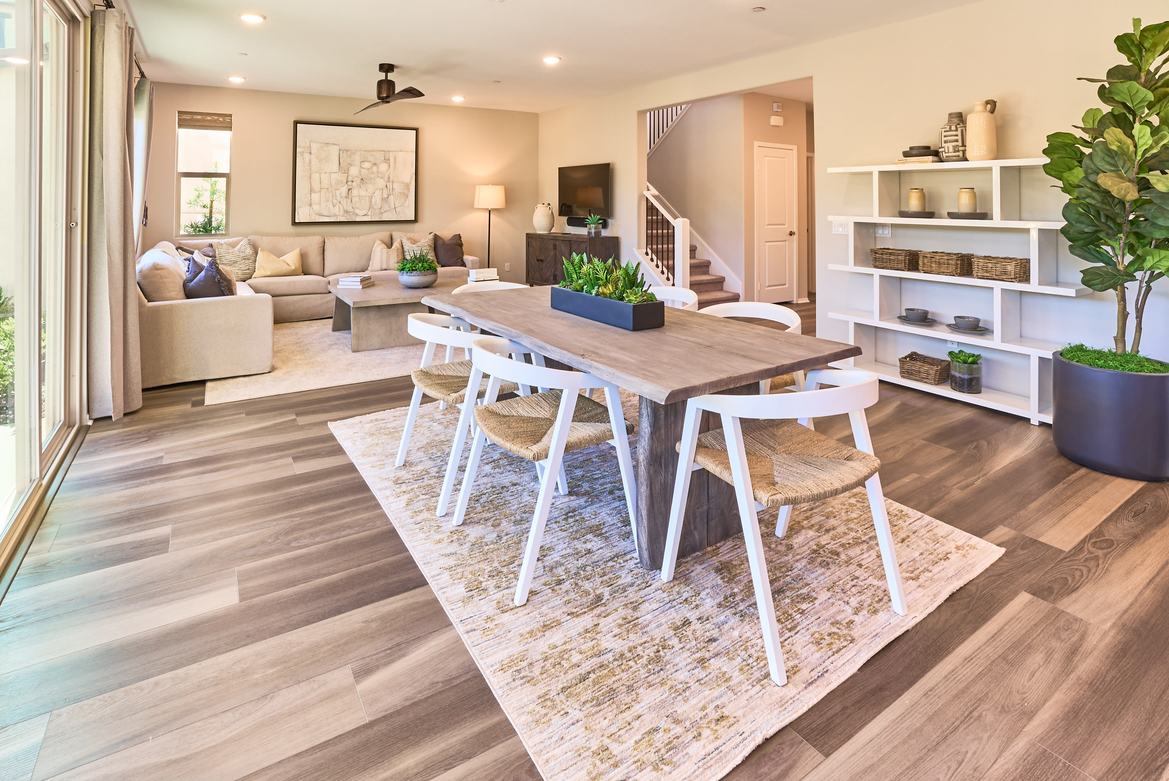 A cozy and inviting living room with a wooden dining table, white chairs, and a comfortable sofa set against a backdrop of shelves, plants, and artwork, creating a warm and harmonious atmosphere.