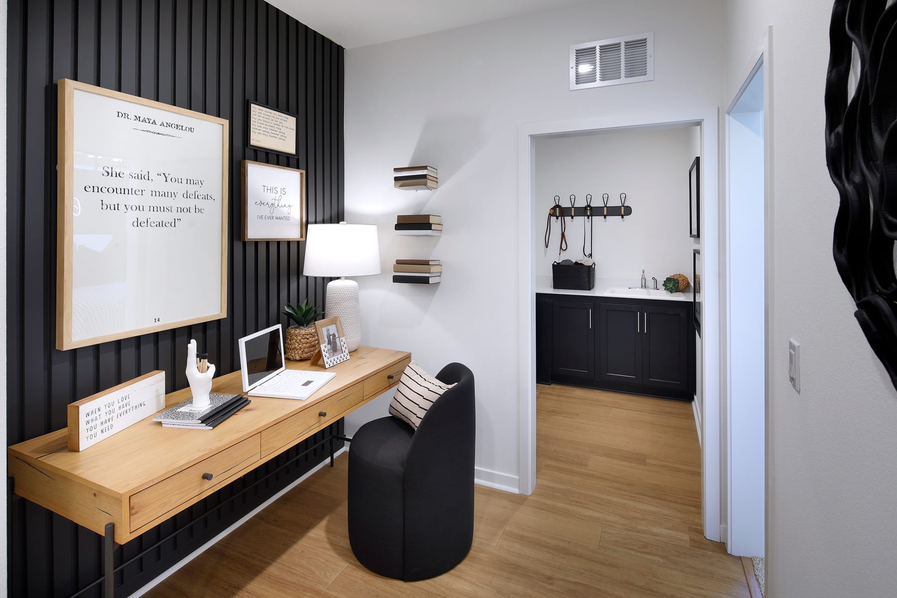 A modern and minimalist home office space with a wooden desk, black chairs, and a framed artwork on the wall, complemented by a black accent wall and open shelving in the background.