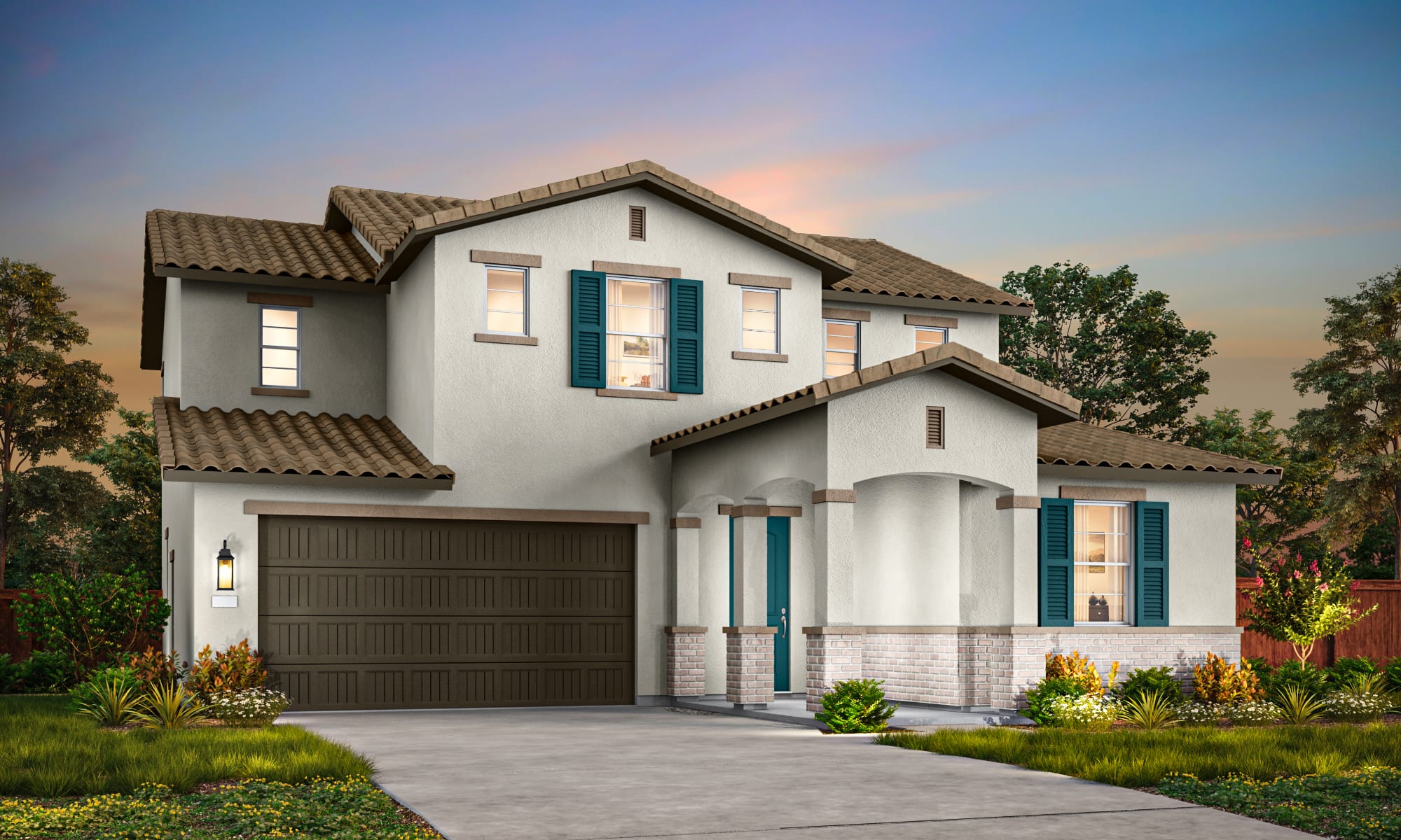A two-story Mediterranean-style house with a tiled roof, a garage door, and a well-manicured lawn with flowering plants in the foreground, set against a backdrop of a blue sky with wispy clouds.