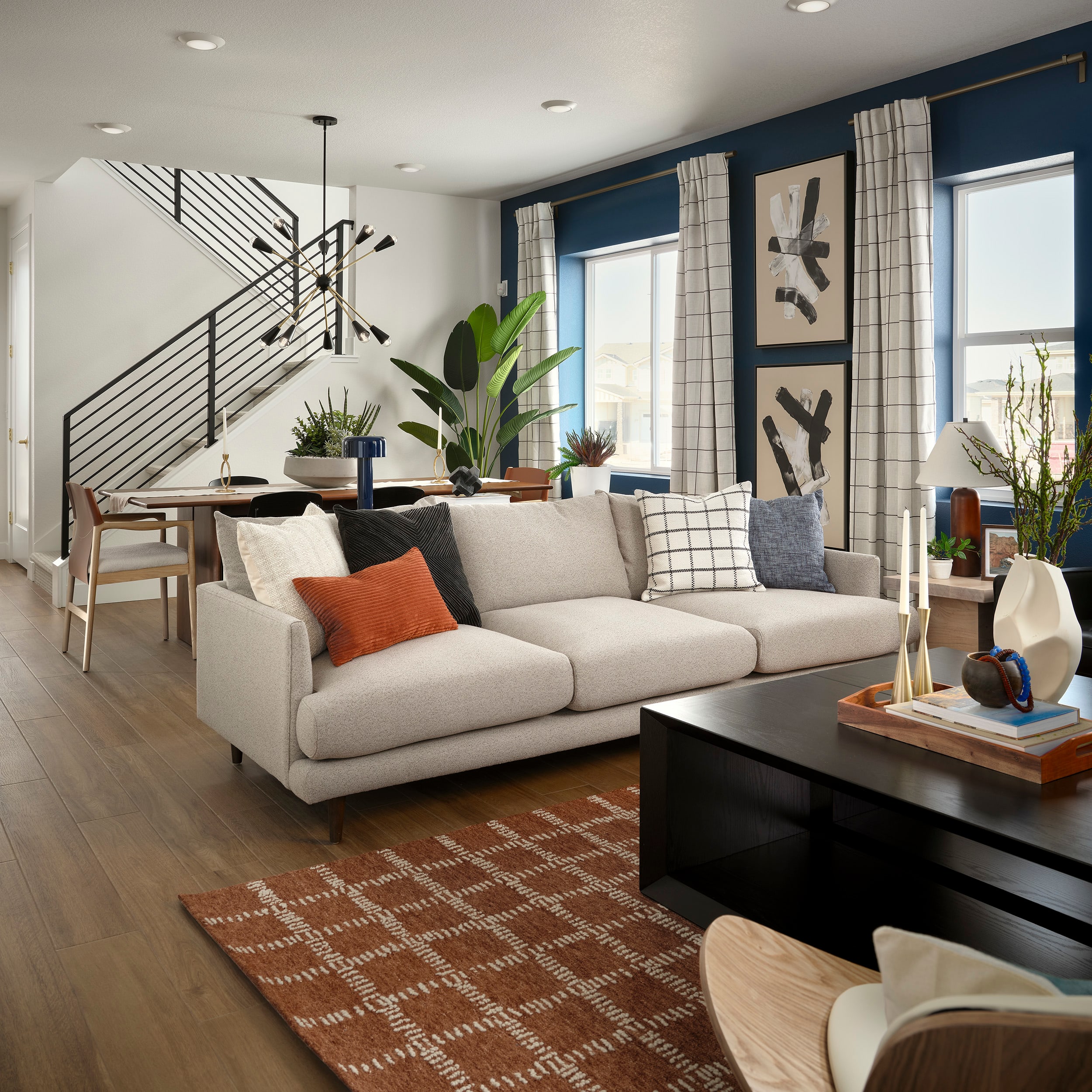 A cozy and modern living room with a large beige sofa, a wooden coffee table, and various decorative elements such as plants, artwork, and textured rugs, creating a warm and inviting atmosphere.