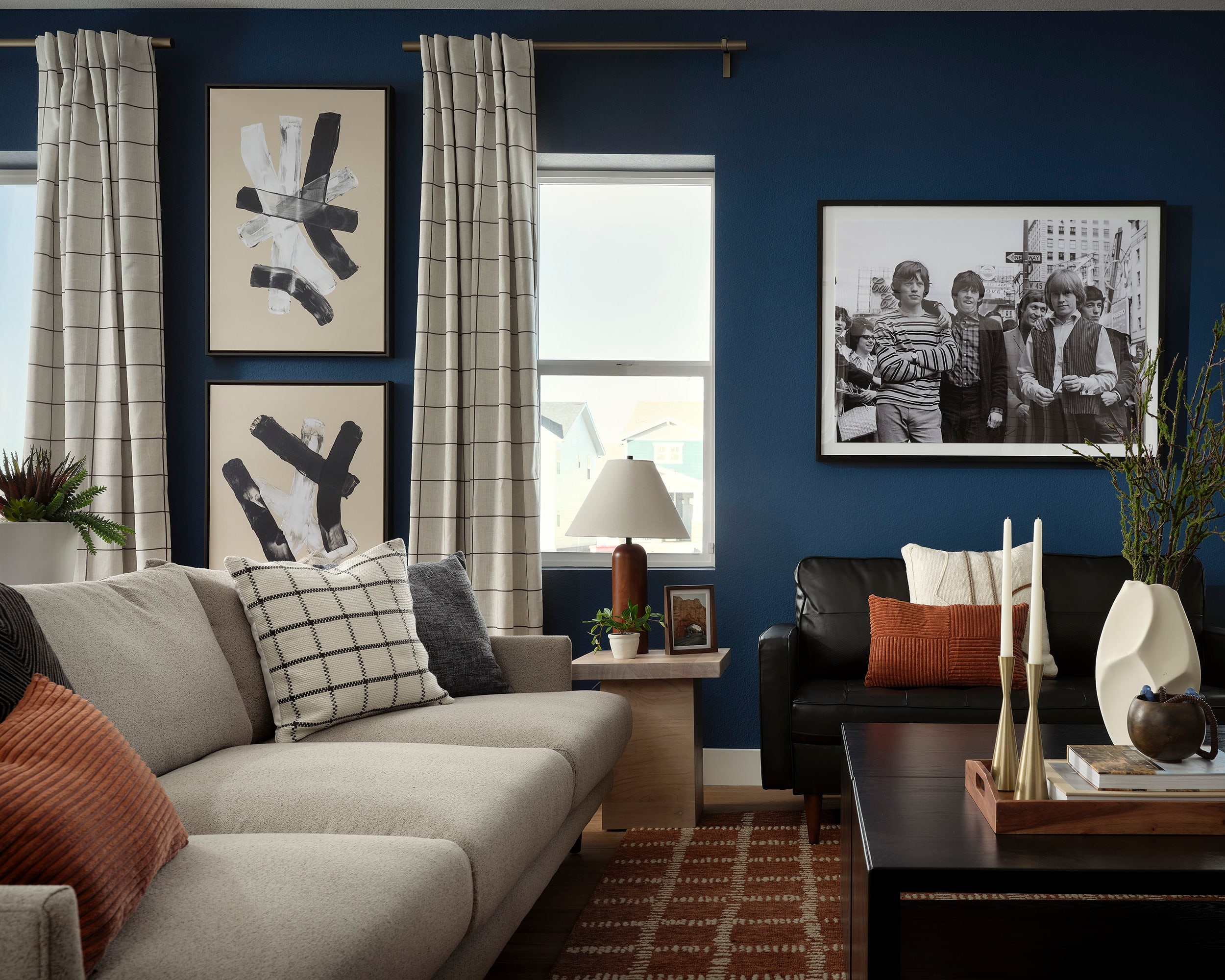 A cozy living room with a gray sofa, patterned rug, and framed artwork on the walls, complemented by a wooden side table and potted plants.