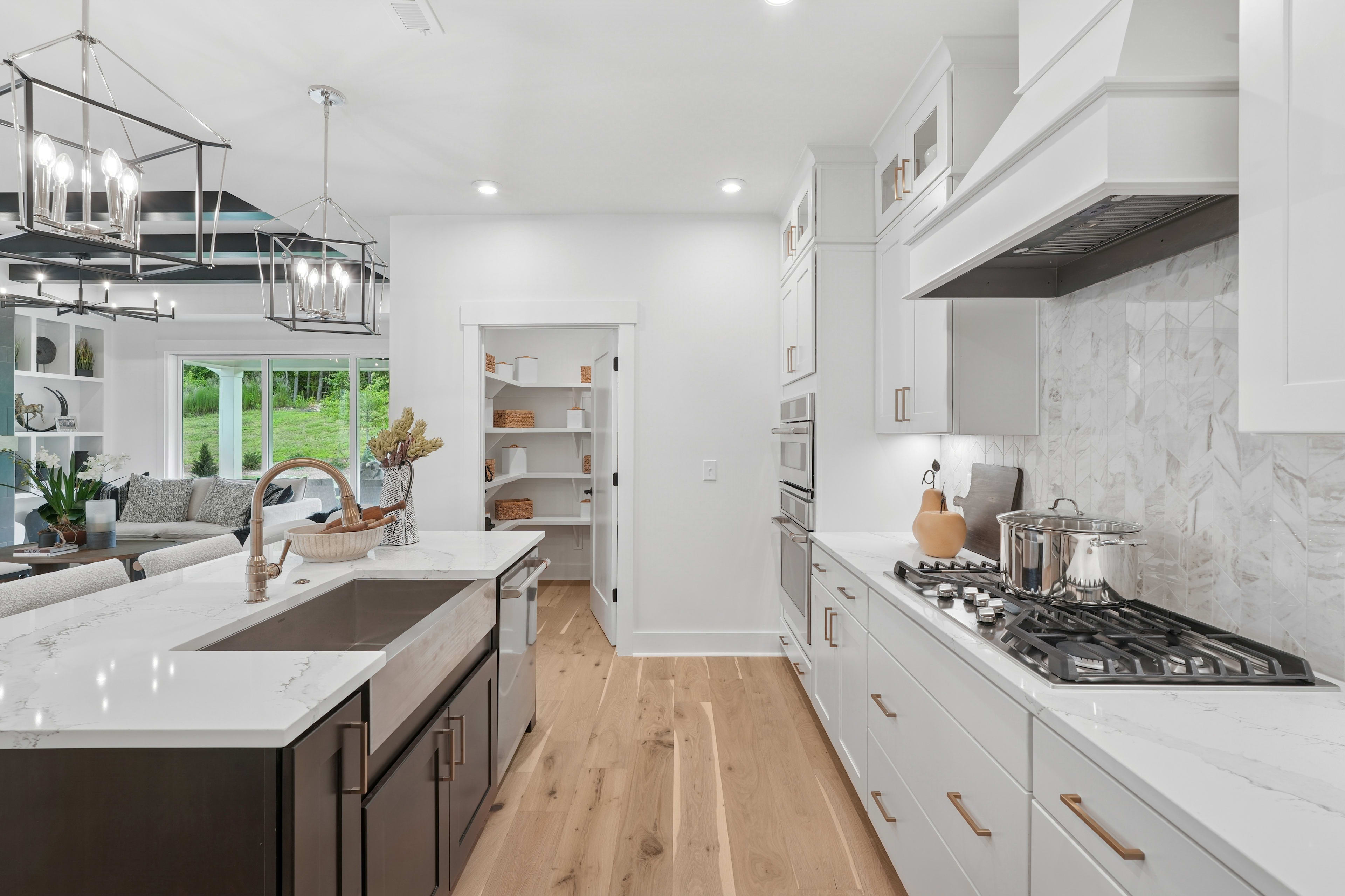 A modern, open-concept kitchen with white cabinets, a marble countertop, and a gas stove, leading into a living room area with a couch and shelving.