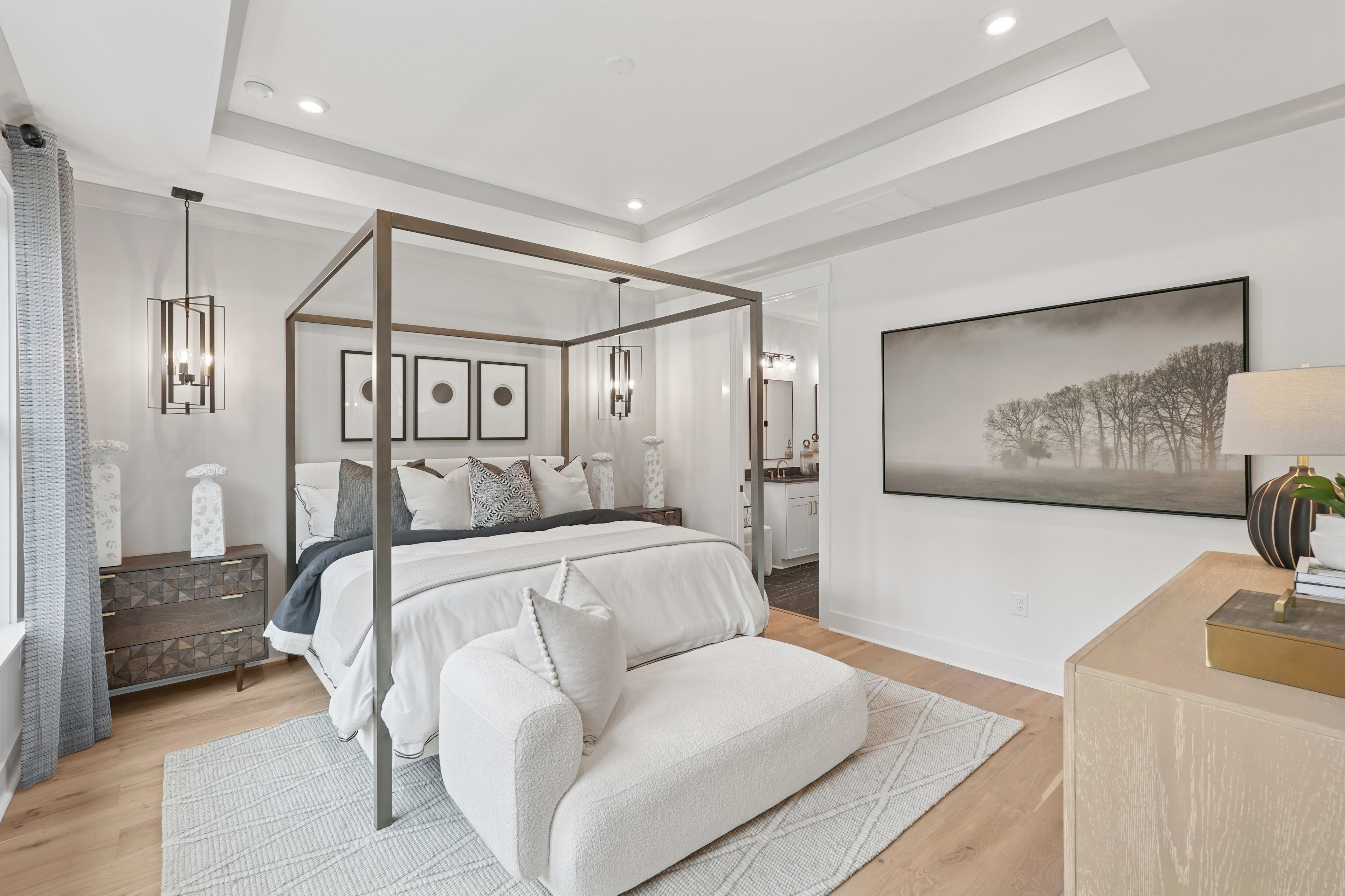 A spacious and elegantly designed bedroom with a canopy bed, neutral-toned decor, and a large framed artwork on the wall.