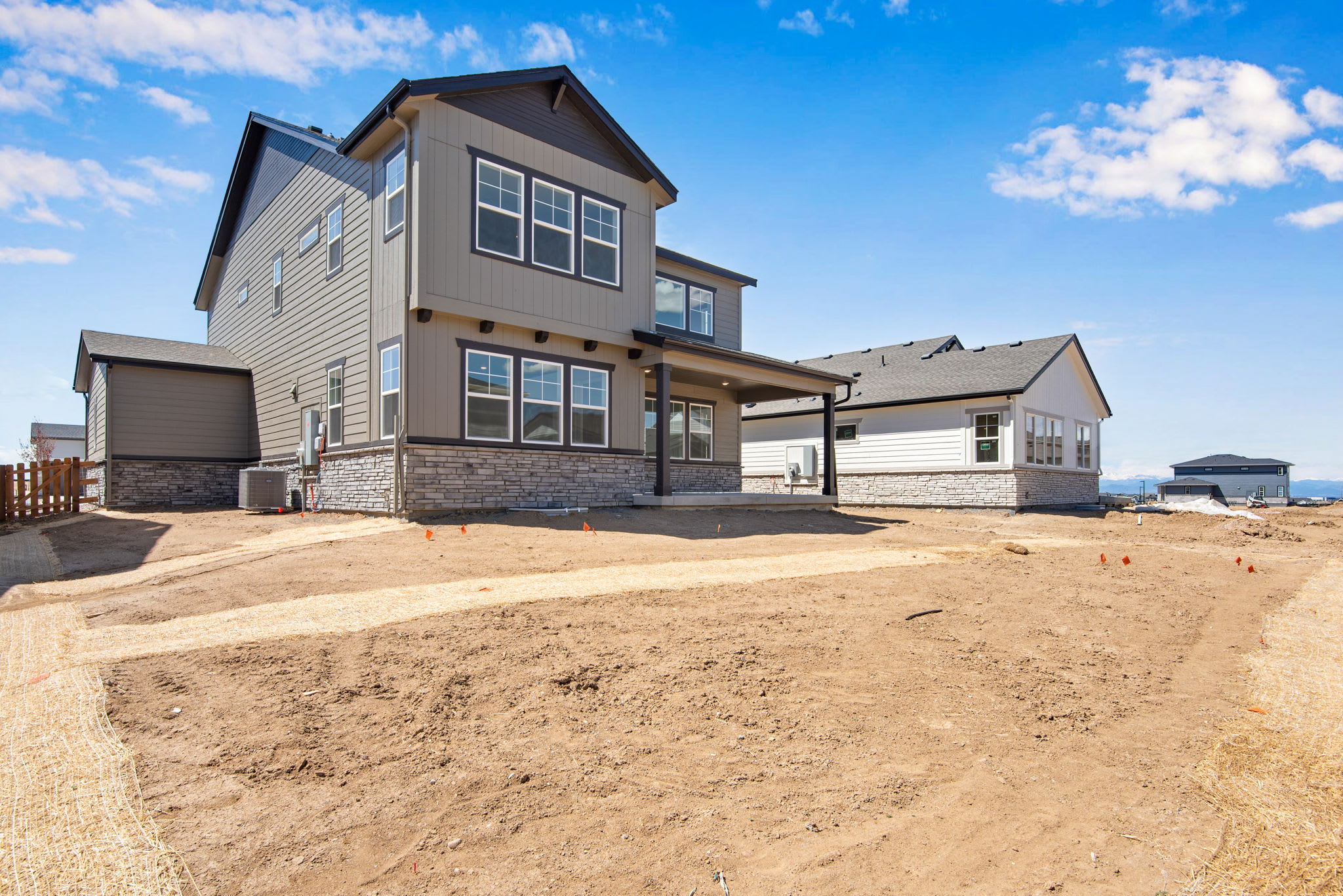 A newly constructed two-story residential home with a gray exterior and a large yard in the foreground, set against a clear blue sky with scattered clouds.