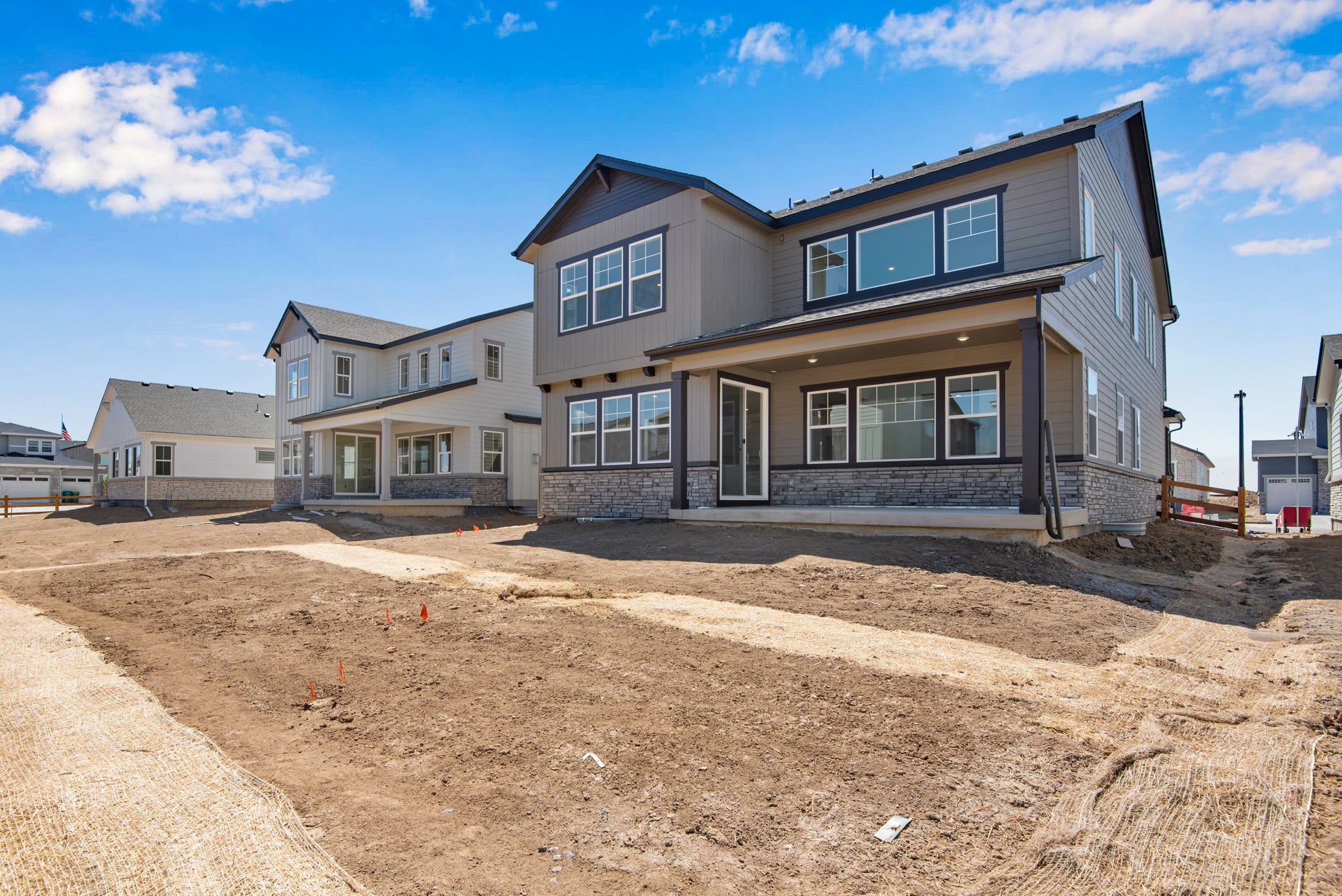 A newly constructed multi-story residential building with a partially completed landscaped yard in the foreground, set against a clear blue sky with scattered clouds.