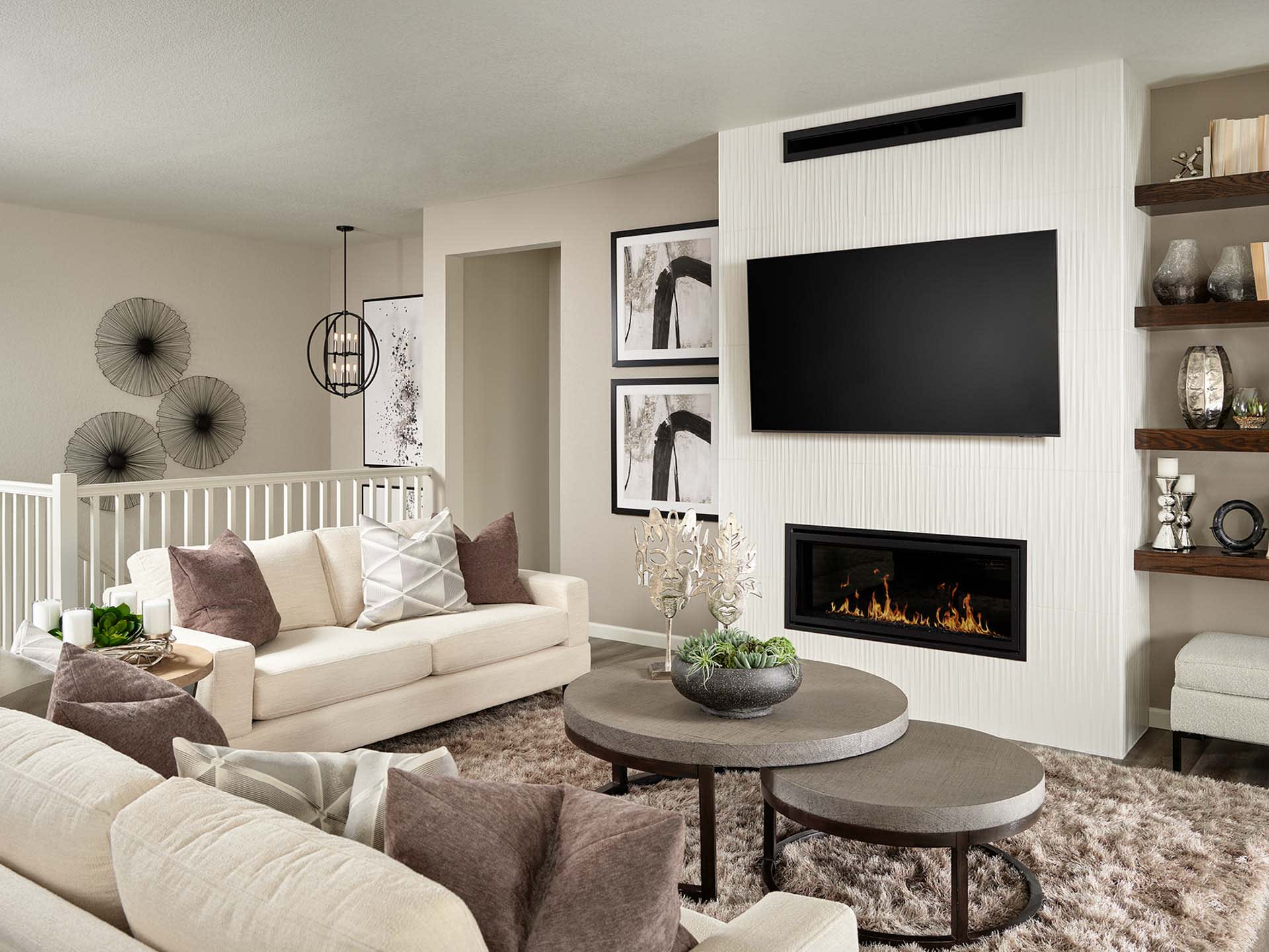 A cozy and modern living room with a white sofa, a fireplace, and a large TV mounted on the wall, surrounded by decorative elements and a coffee table with nesting tables.