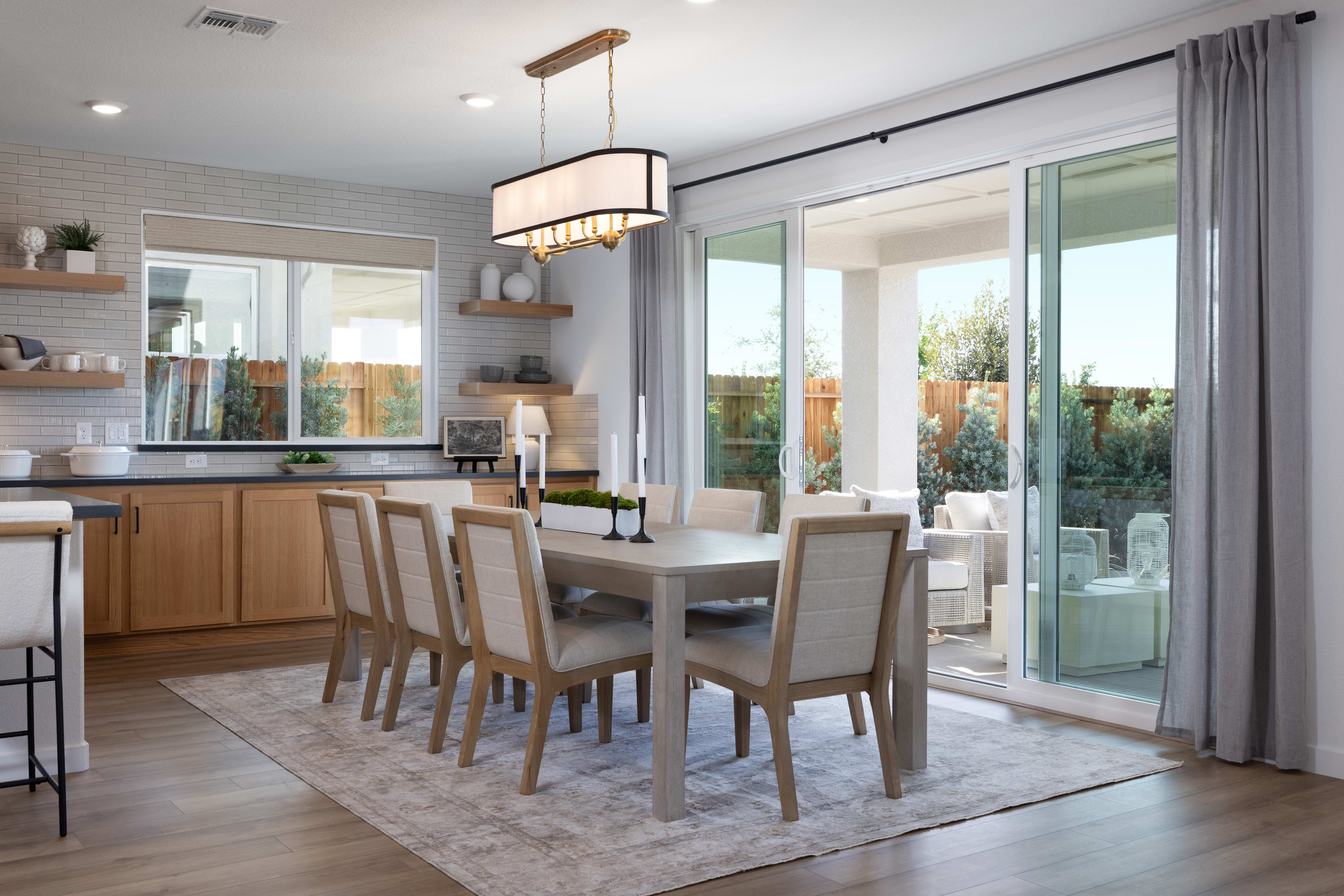 A modern and spacious dining room with a wooden table, upholstered chairs, and a large window overlooking a lush outdoor area.