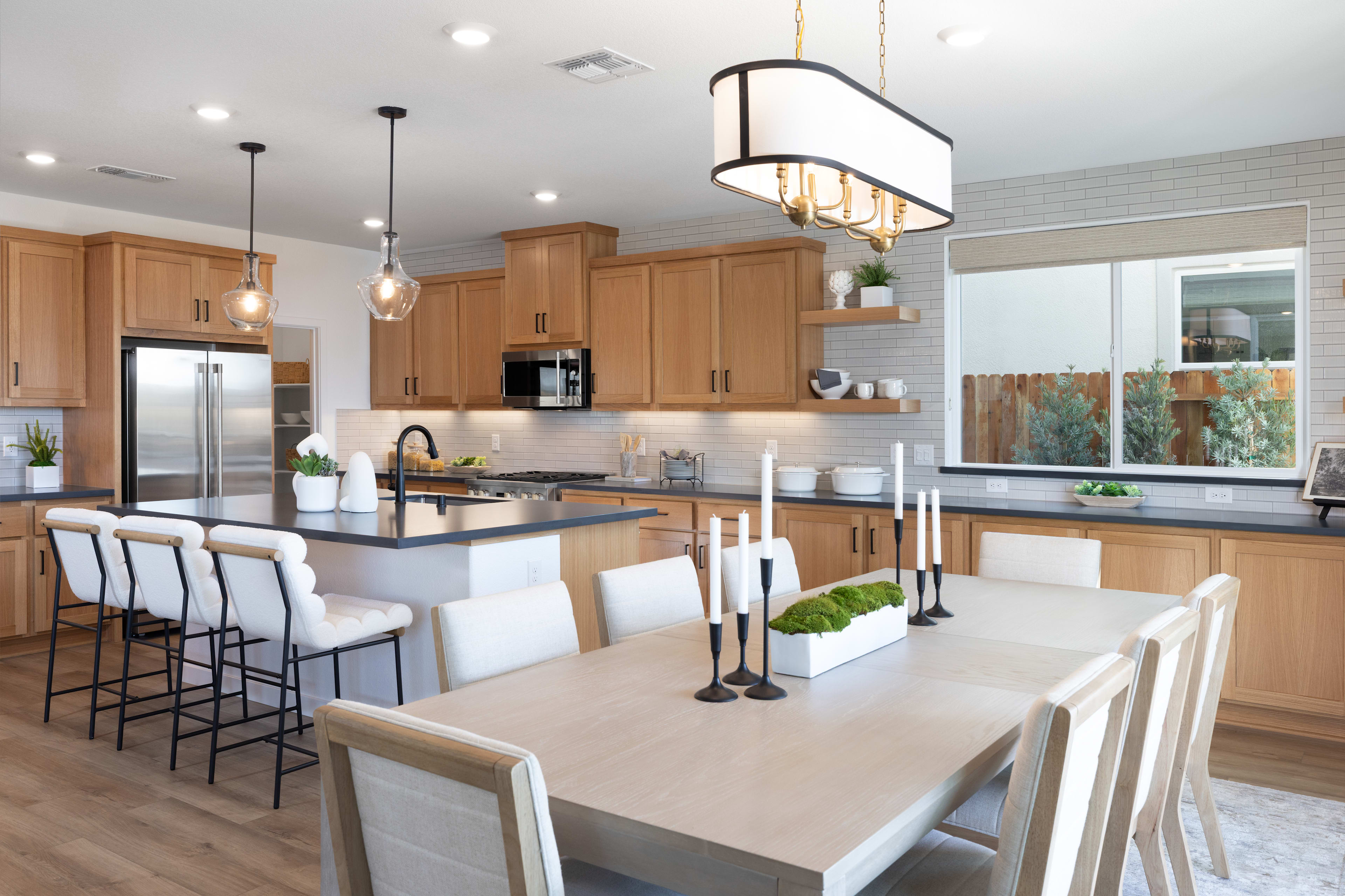 A modern and spacious kitchen with wooden cabinets, a large dining table, and a central island with bar stools, all illuminated by a stylish pendant light fixture.