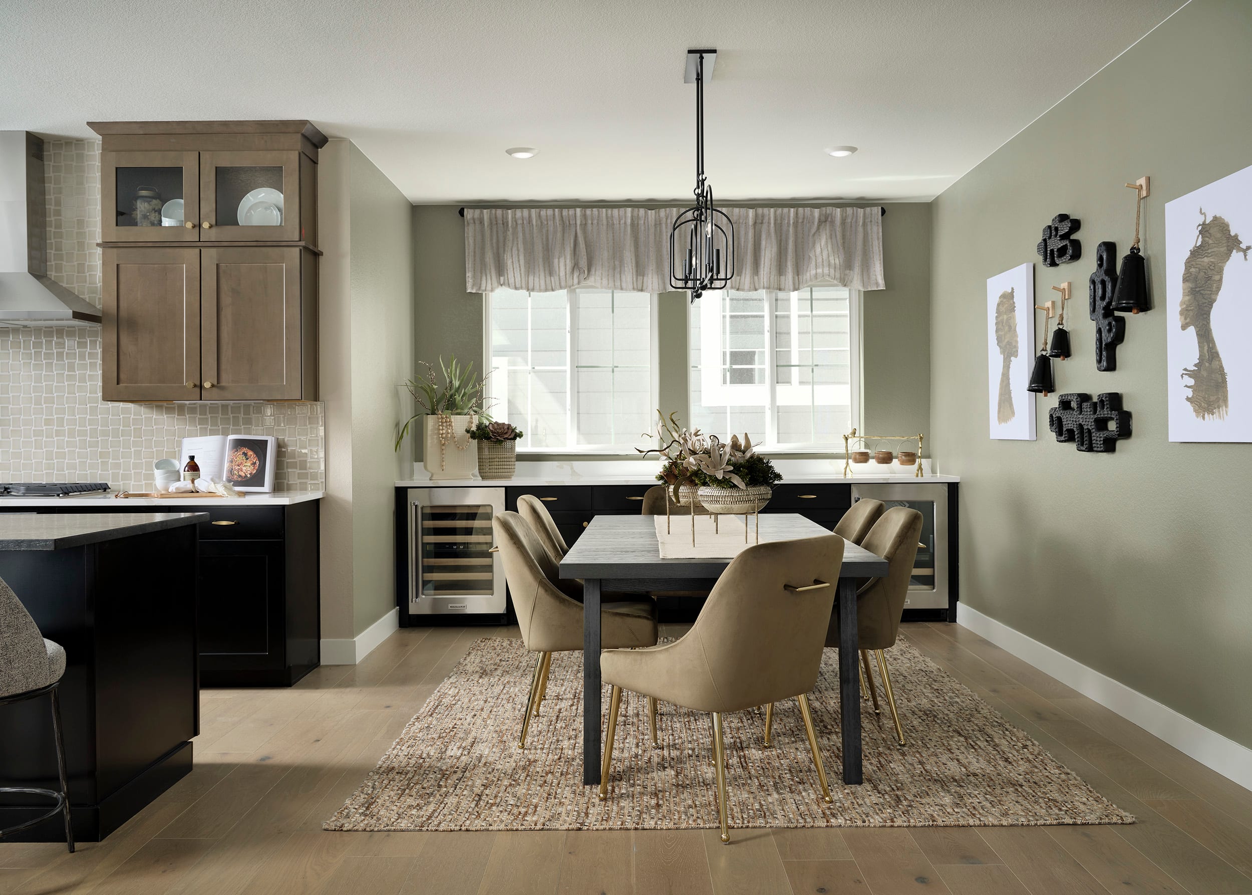 A modern and cozy kitchen-dining area with wooden cabinets, a large dining table surrounded by beige chairs, and a chandelier hanging overhead.