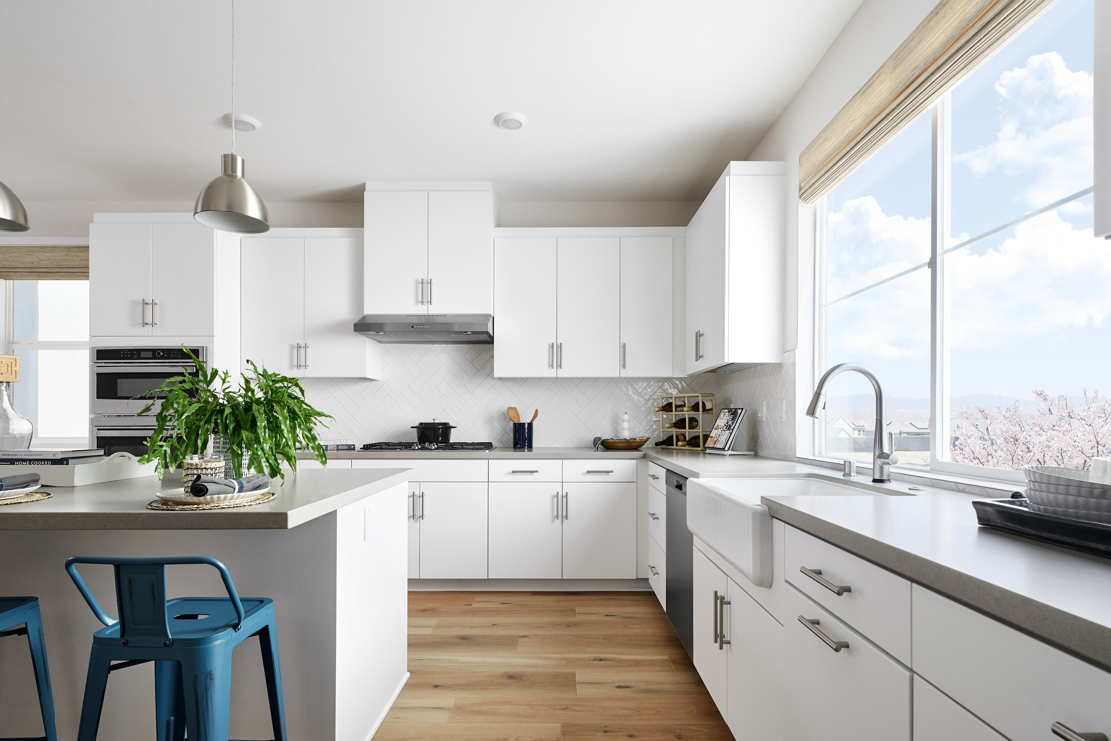 A modern, bright, and spacious kitchen with white cabinets, stainless steel appliances, and a large window overlooking a scenic outdoor view.