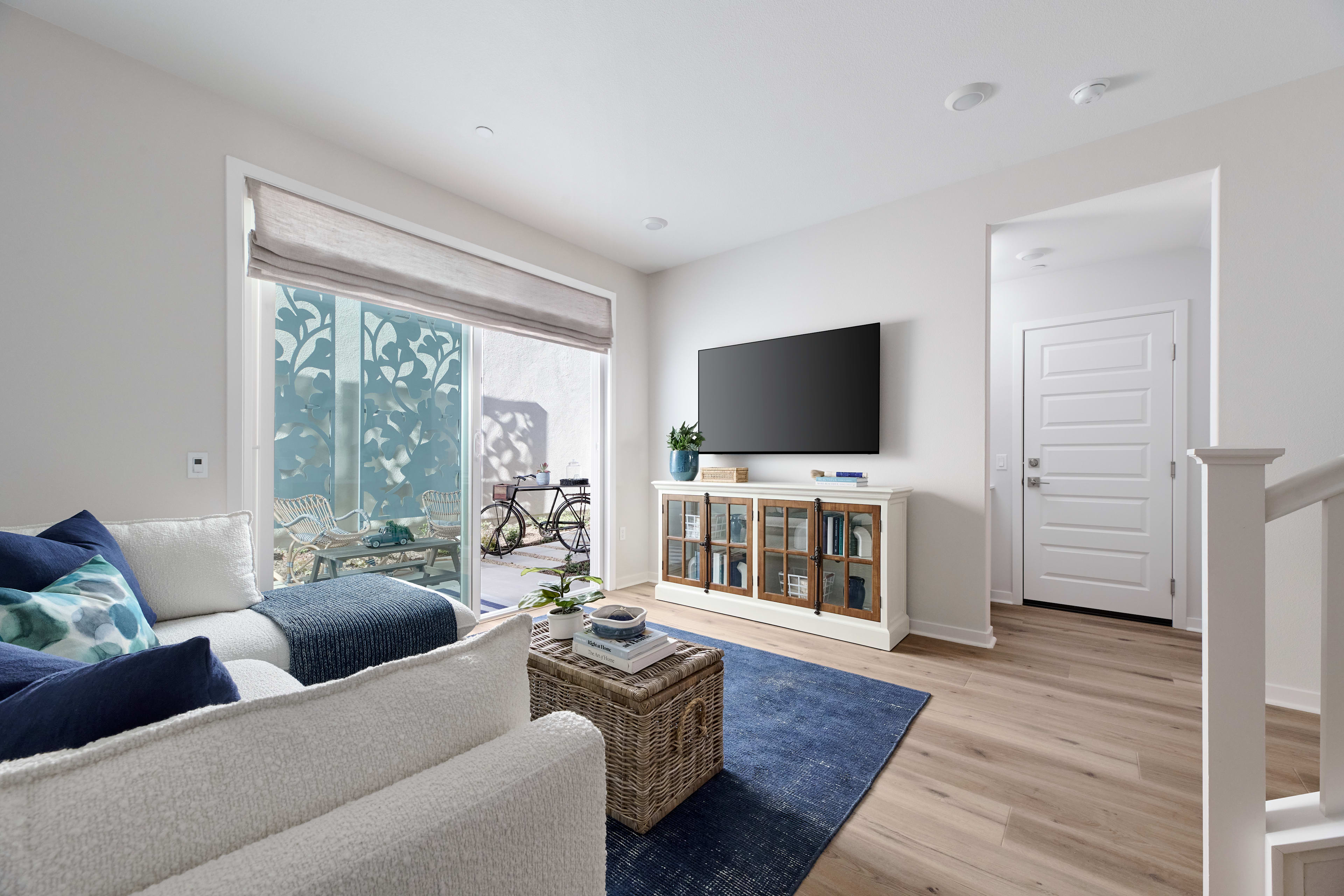 A cozy and modern living room with a large window, a gray sofa, a wooden cabinet, and a blue rug on the hardwood floor.