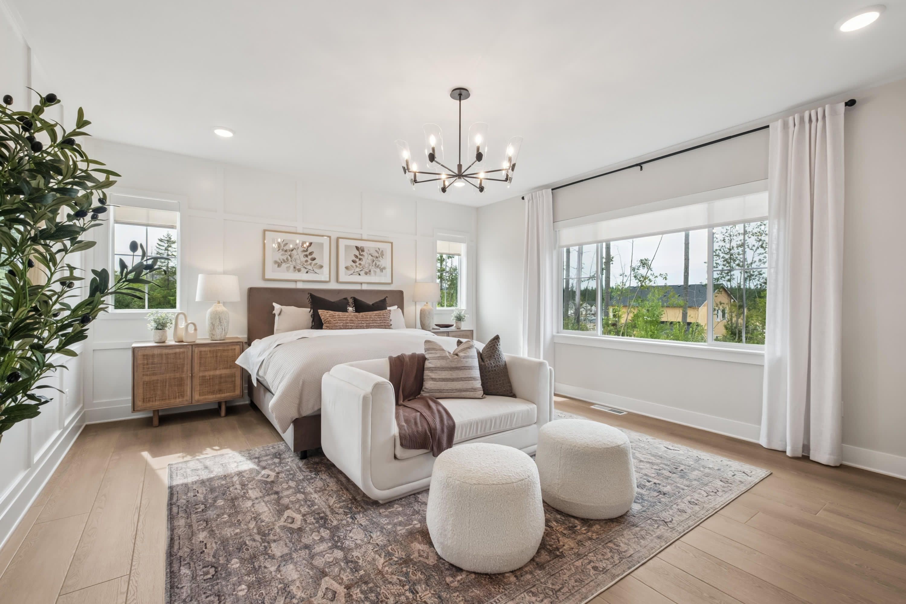 A spacious and elegantly decorated bedroom with a large window, a plush armchair, and a chandelier hanging from the ceiling, creating a warm and inviting atmosphere.