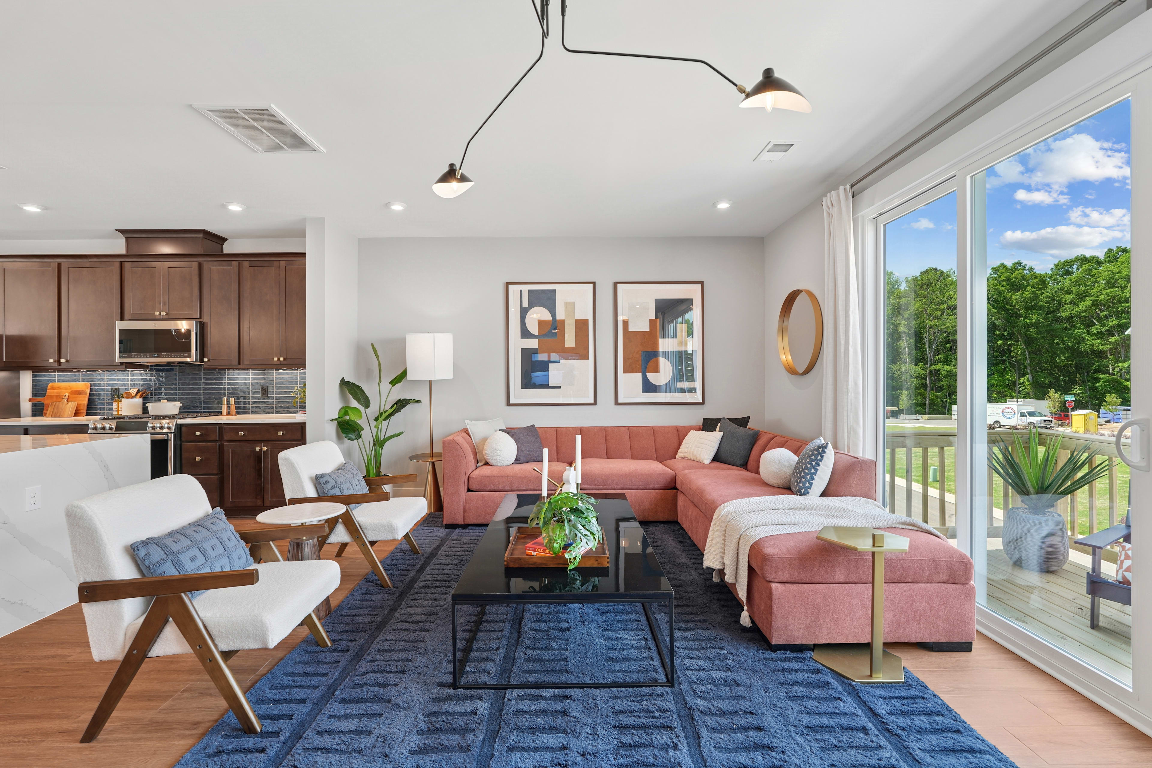 A modern and cozy living room with a pink sofa, wooden furniture, and large windows overlooking a lush outdoor scene.