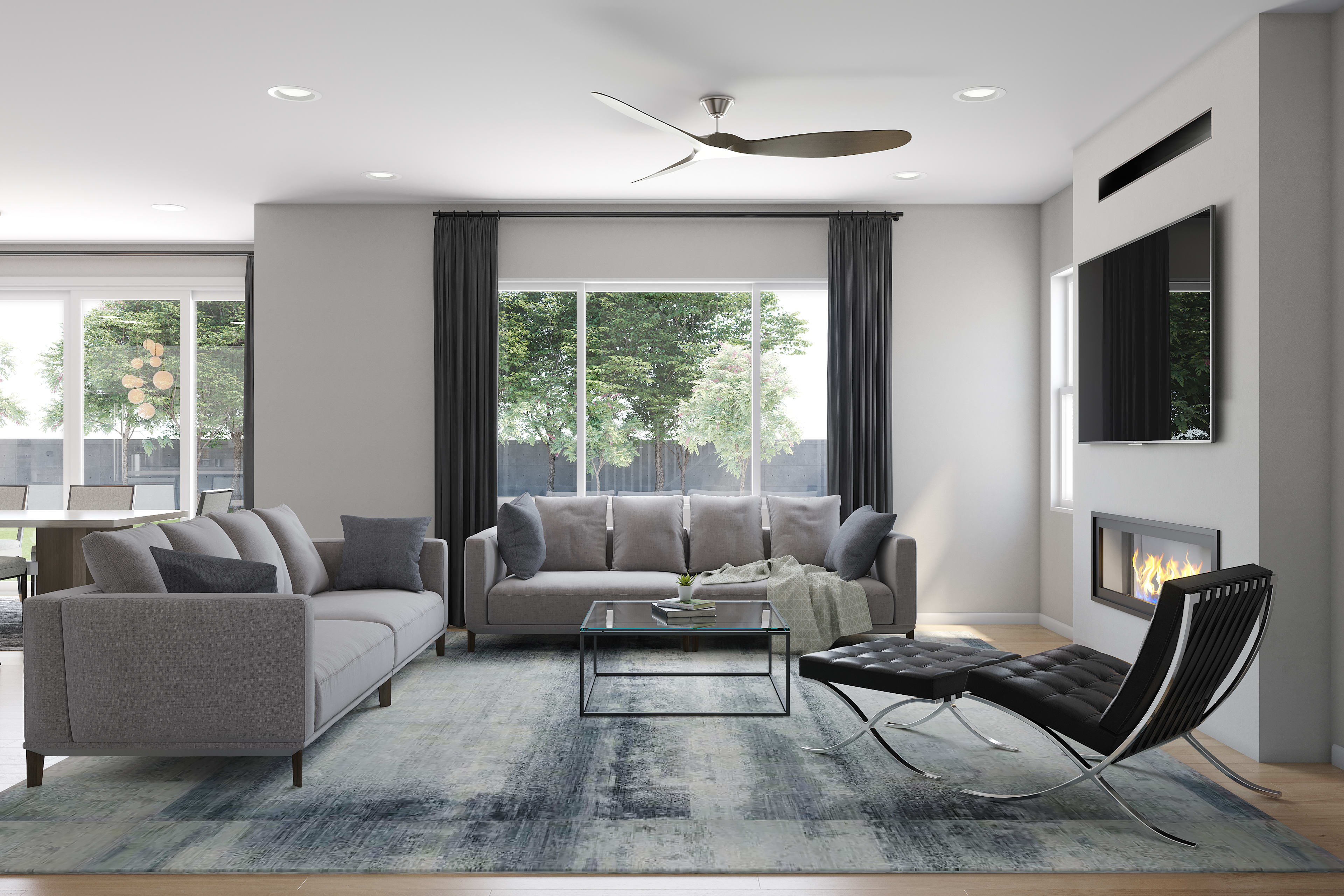 A modern and minimalist living room with gray sofas, a glass coffee table, and a Barcelona chair set against a backdrop of large windows overlooking a lush outdoor environment.