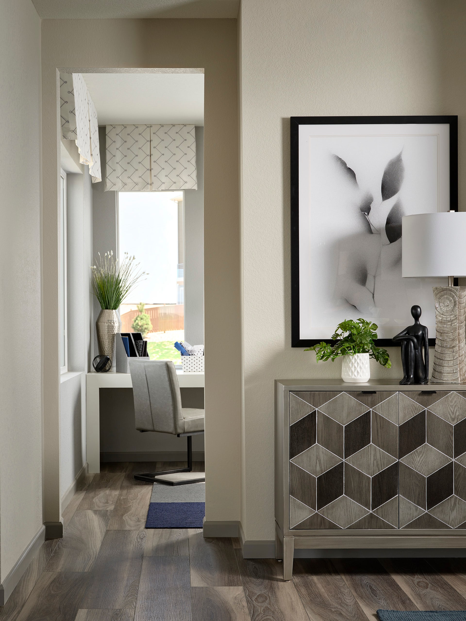 A modern and minimalist living room with a geometric patterned cabinet, a framed abstract artwork, and a cozy seating area visible in the background.