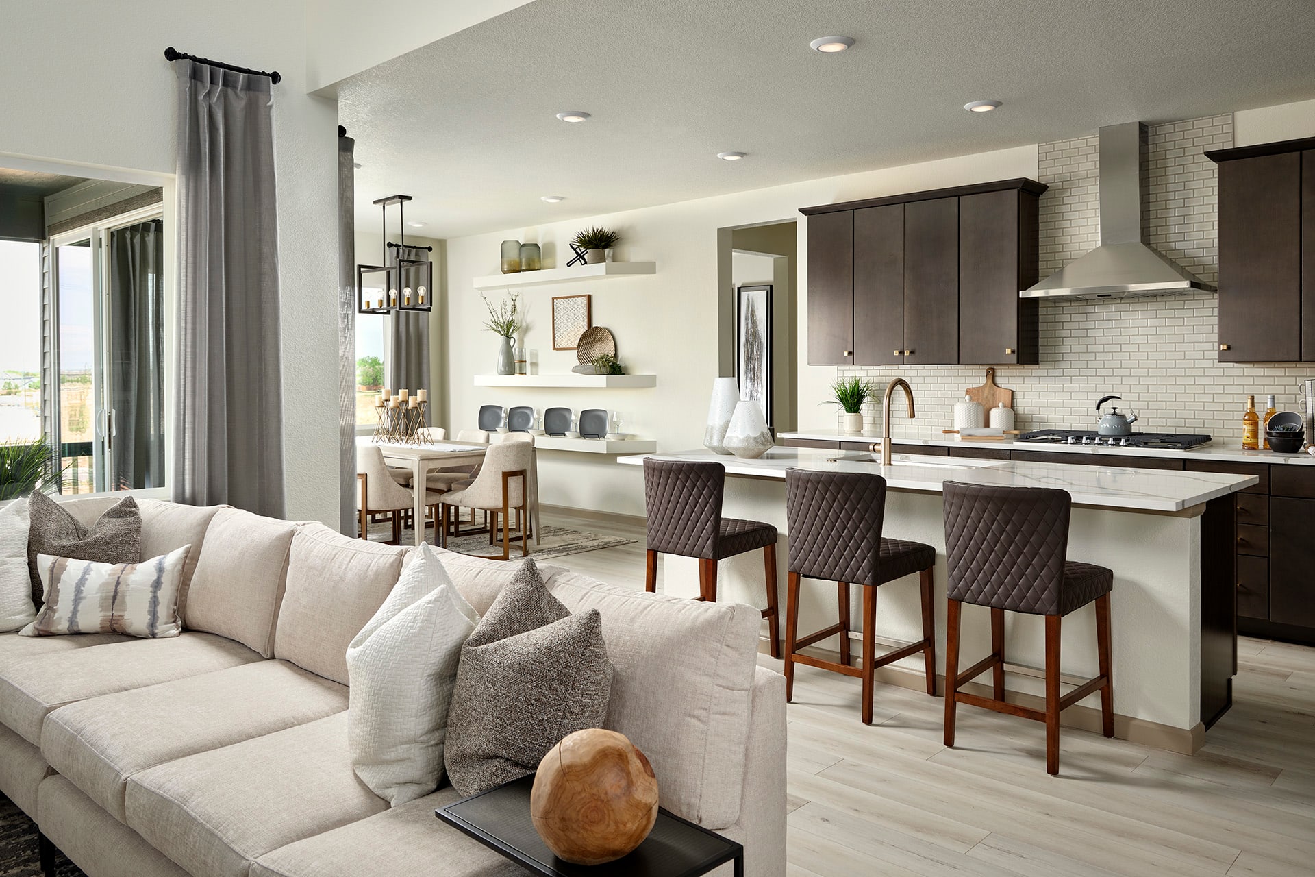 A cozy and modern open-concept living room and kitchen area with a large white sectional sofa, dark wood cabinetry, and a breakfast bar with stools.