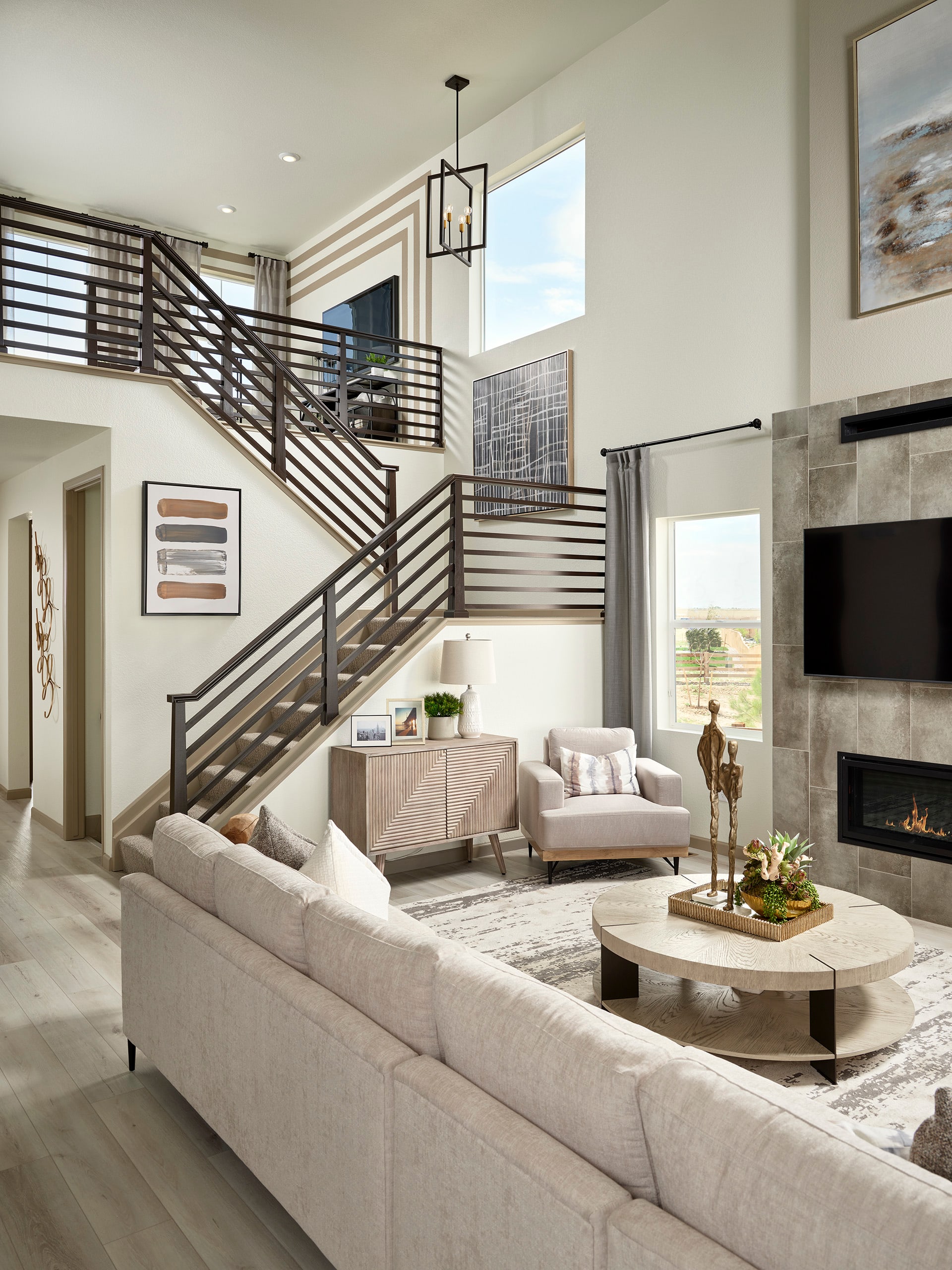 A modern and spacious living room with a cozy seating area, a fireplace, and a staircase leading to an upper level, all bathed in natural light from the large windows.