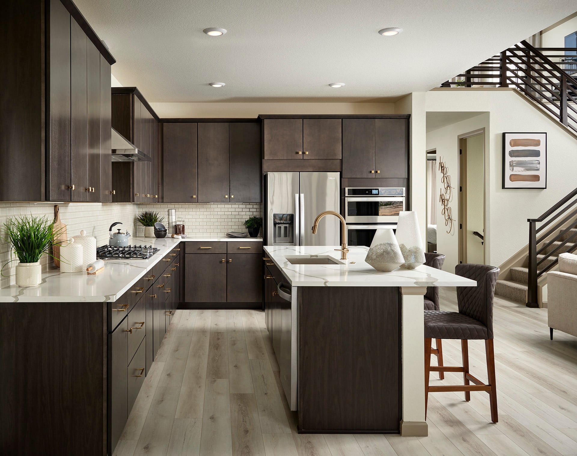 A modern and sleek kitchen with dark wood cabinets, a large island with a white countertop, and stainless steel appliances, set against a backdrop of a bright and open living space.