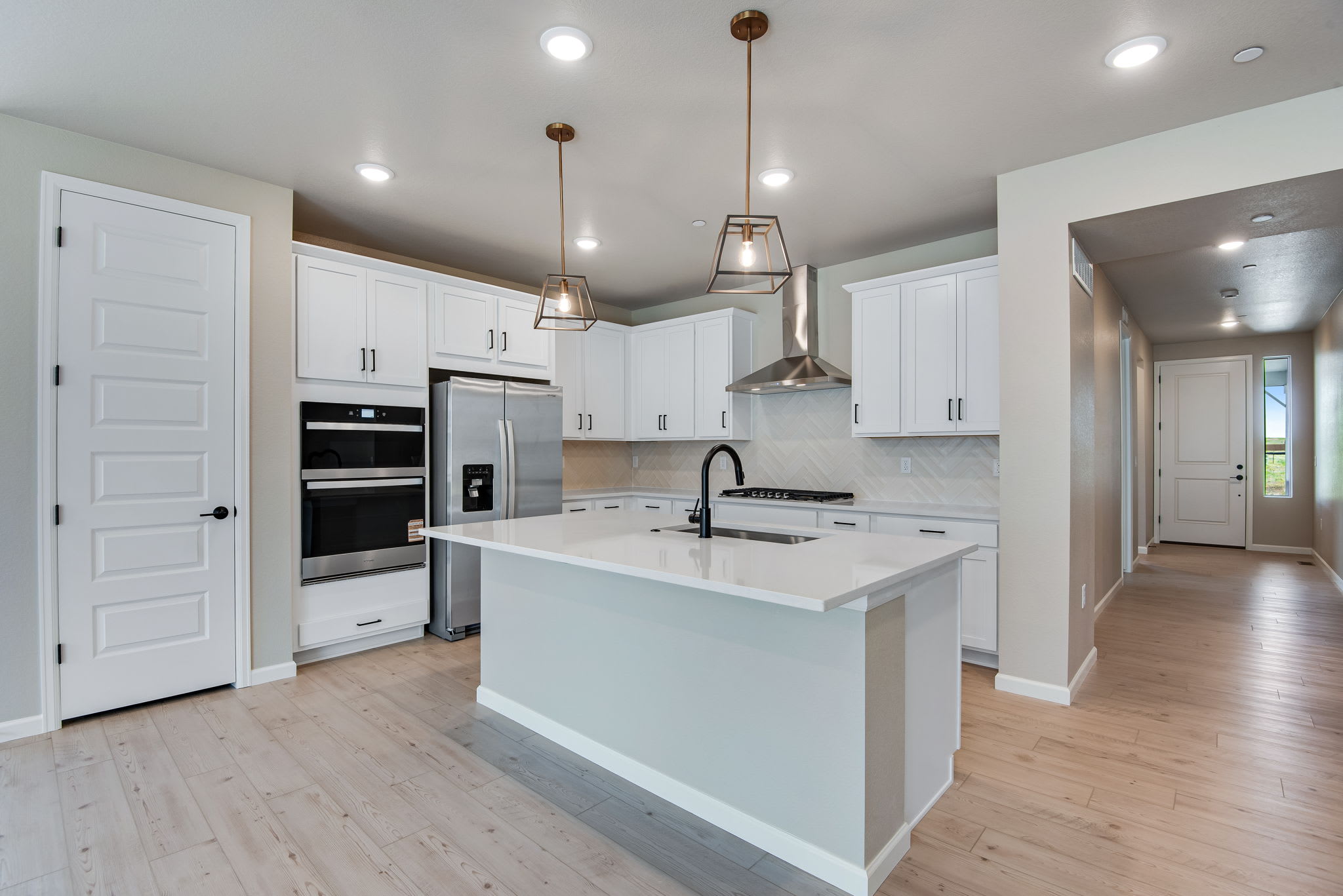A modern, open-concept kitchen with white cabinets, stainless steel appliances, and a central island with a white countertop, set against a light-colored hardwood floor.