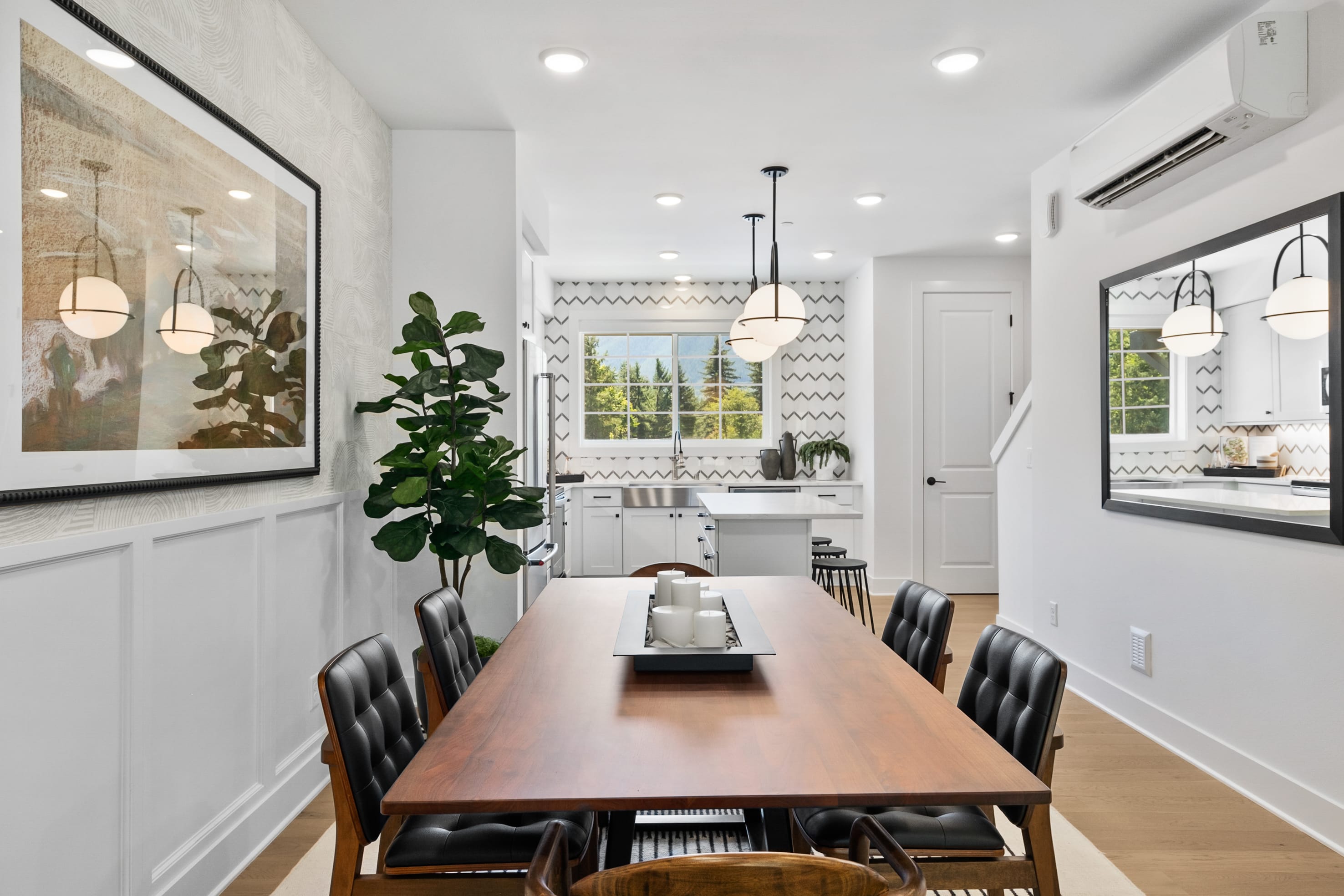 A modern and stylish dining room with a long wooden table, black chairs, and various decorative elements such as a large framed artwork, a potted plant, and pendant lighting fixtures.
