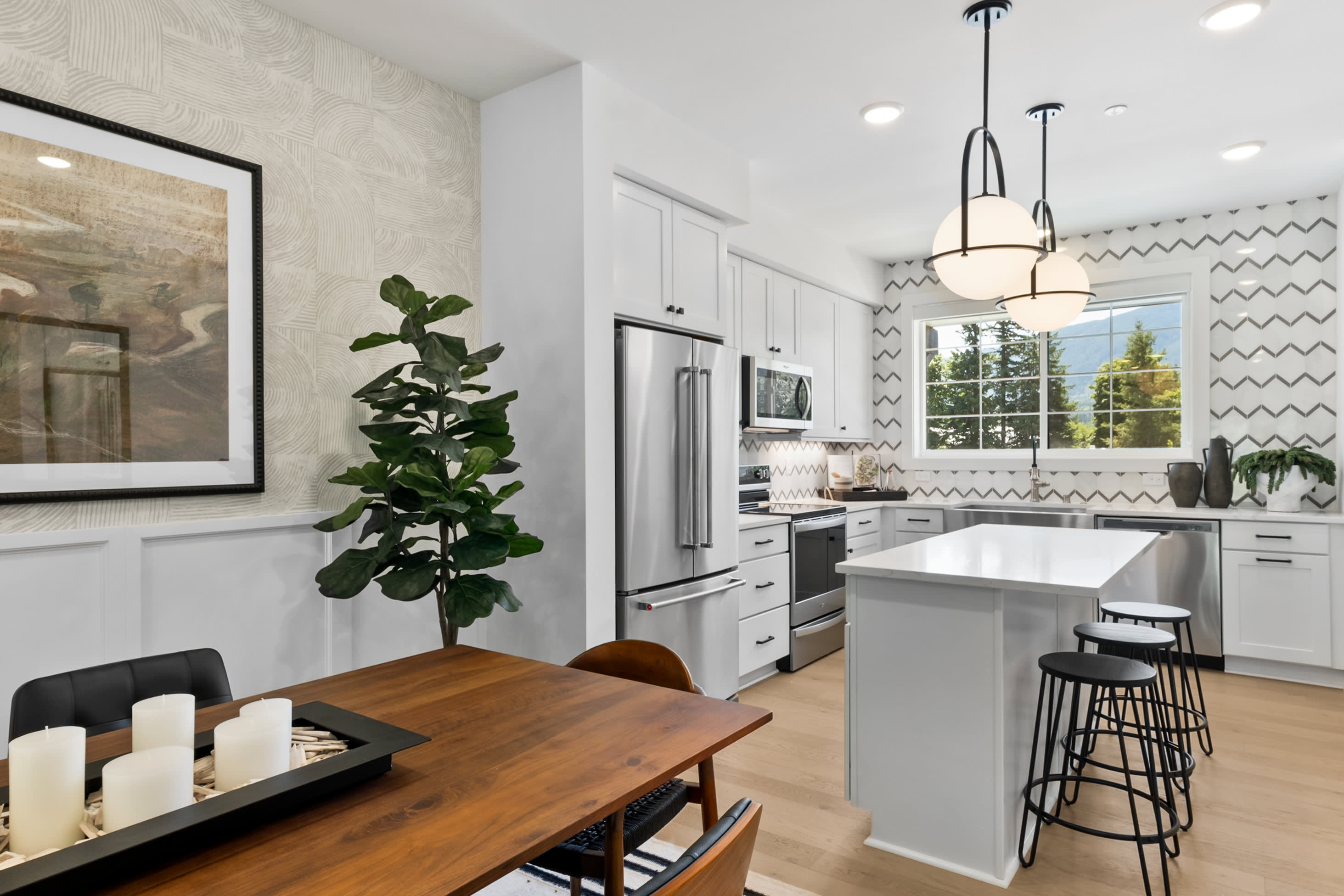 A modern, well-lit kitchen with white cabinets, stainless steel appliances, and a wooden dining table in the foreground.