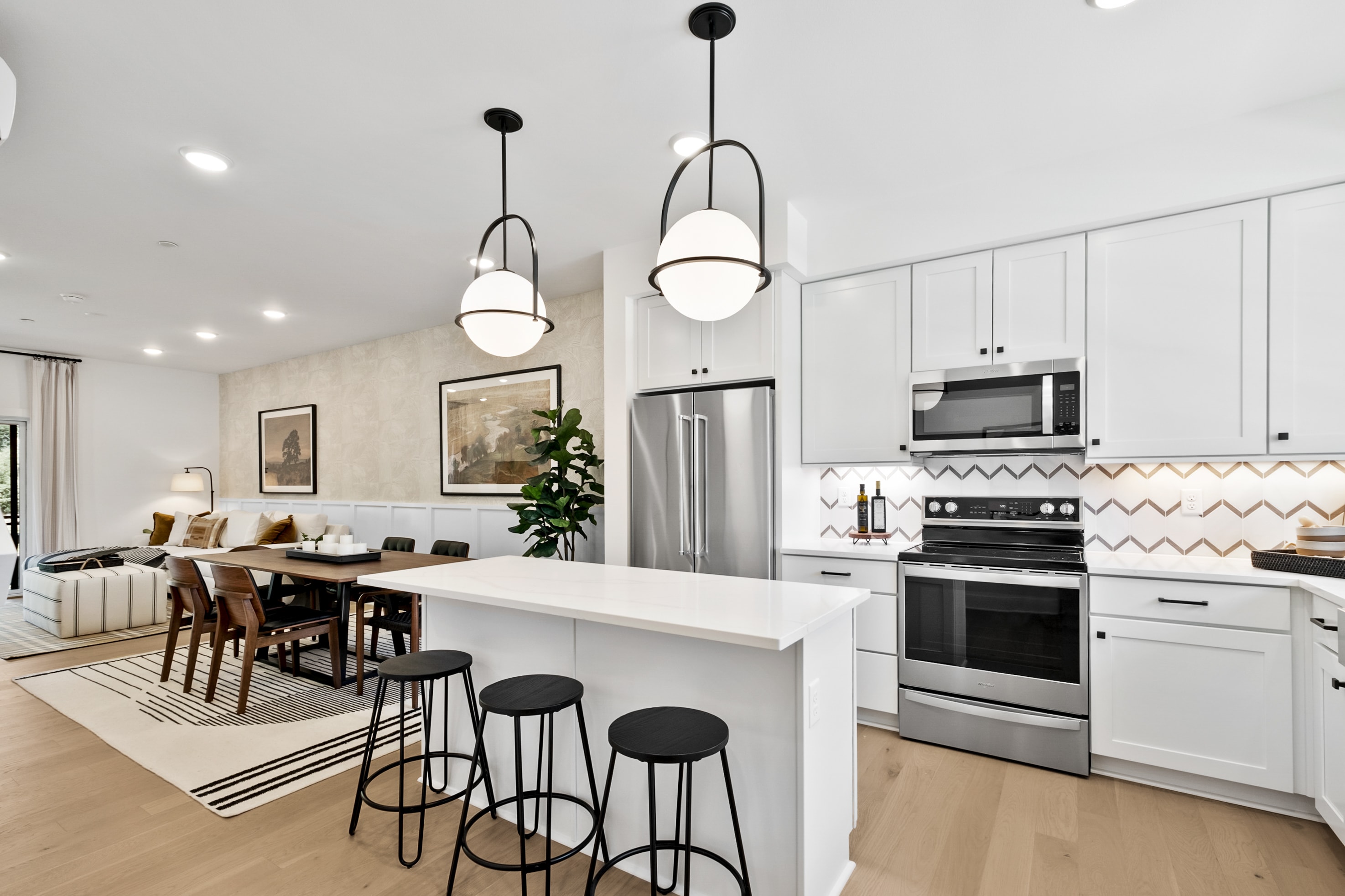 A modern, open-concept kitchen and dining area with white cabinets, stainless steel appliances, and pendant lighting over a central island with bar stools.