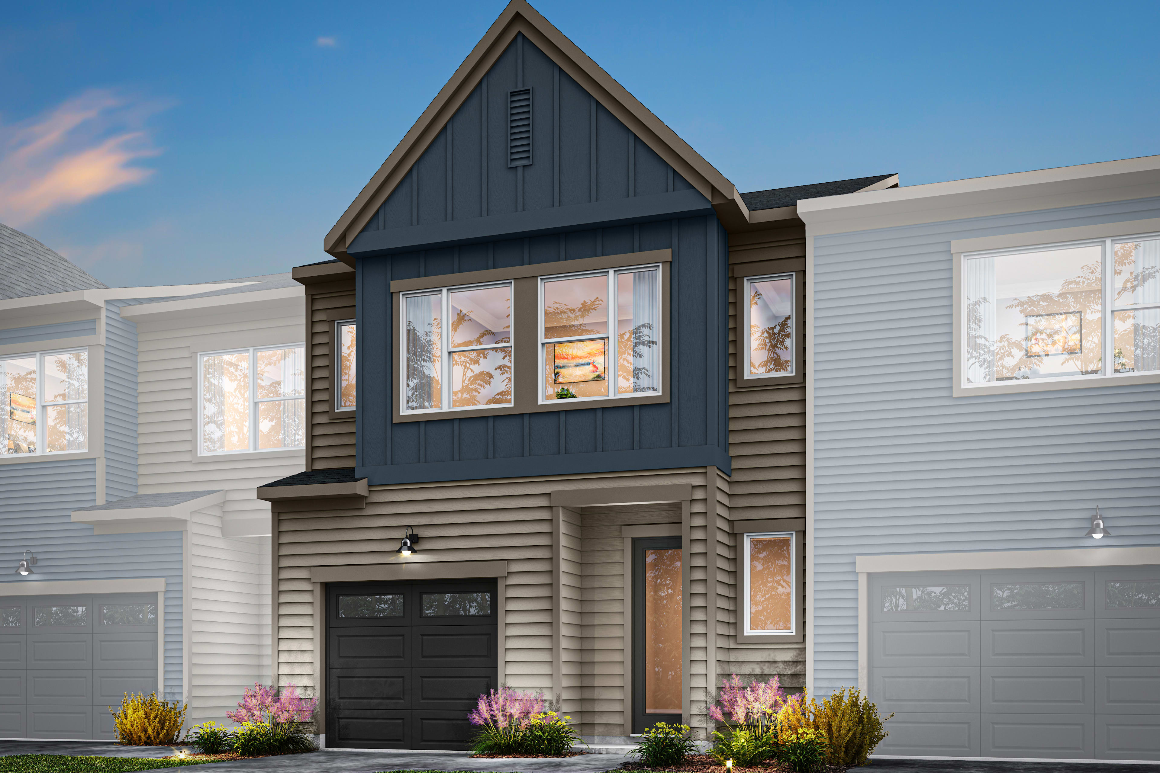 A modern two-story townhouse with a gabled roof, gray siding, and a landscaped front yard featuring colorful flowers.