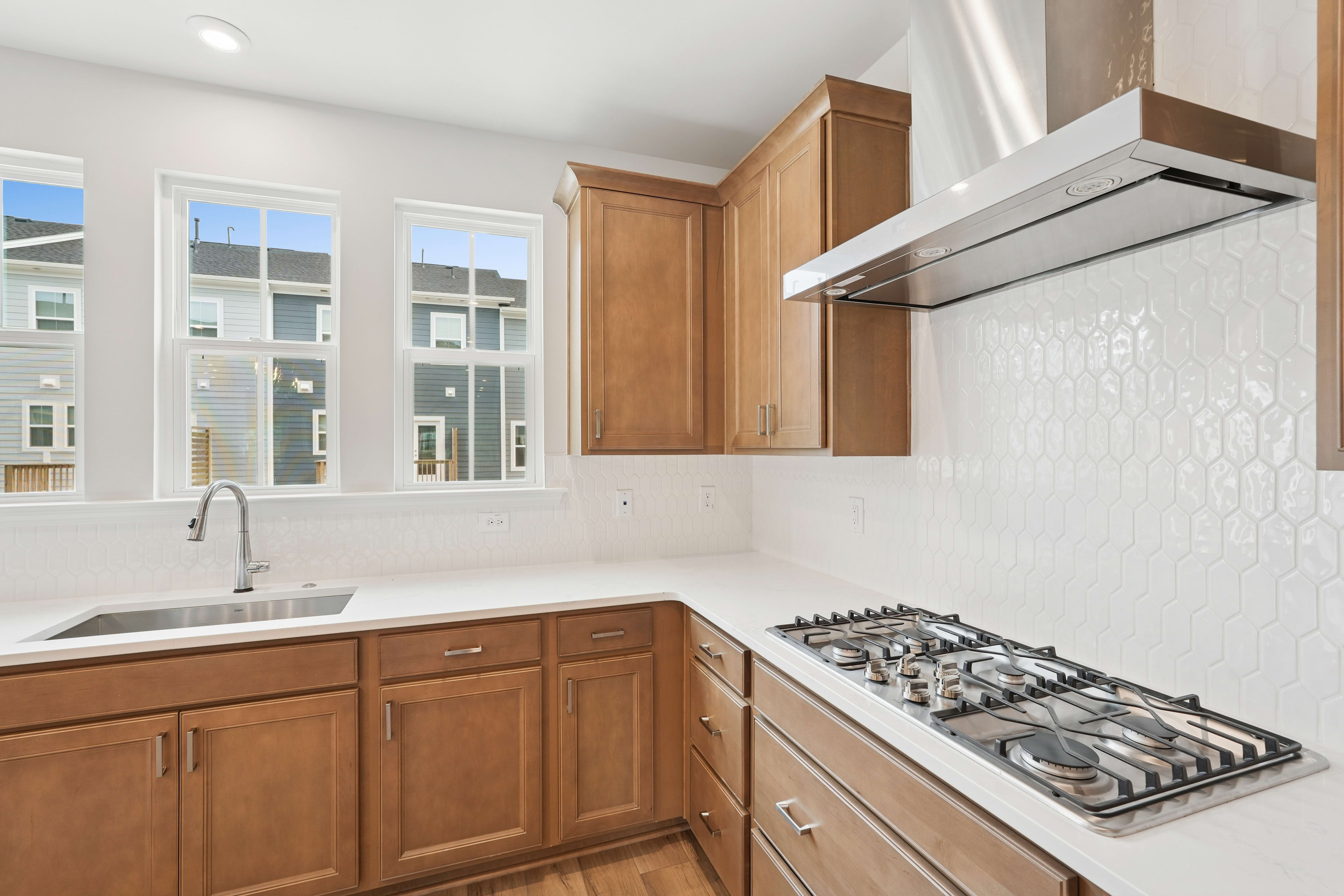 A modern kitchen with wooden cabinets, a gas stove, and large windows providing ample natural light.