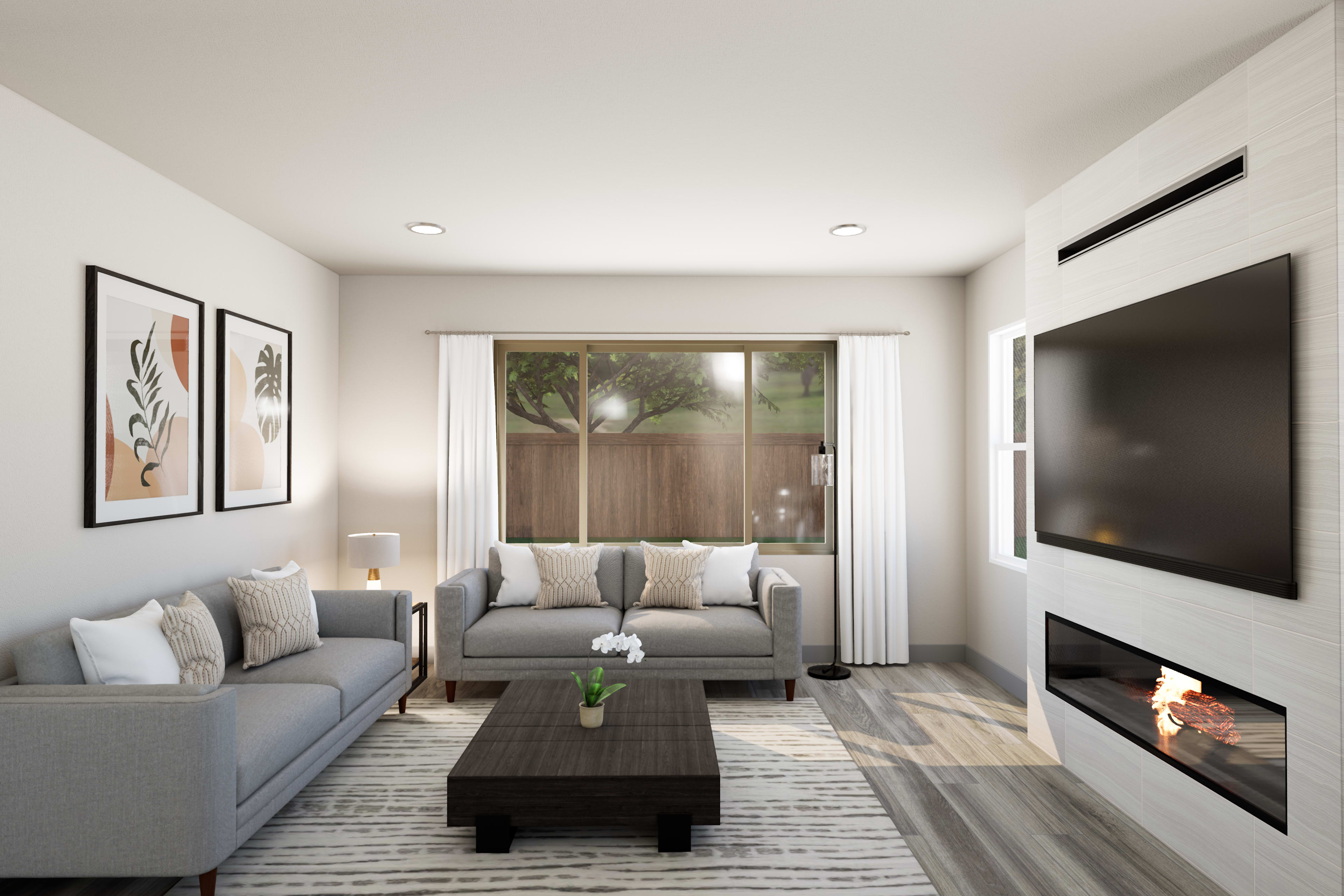 A cozy and modern living room with a gray sofa, a coffee table, and a fireplace, surrounded by framed artwork on the walls and a view of the outdoors through a window.