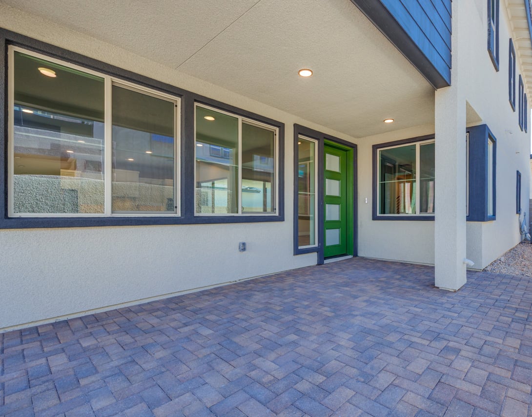 A modern, well-lit building with a paved entrance and large windows, featuring a vibrant green door that stands out against the neutral color scheme.