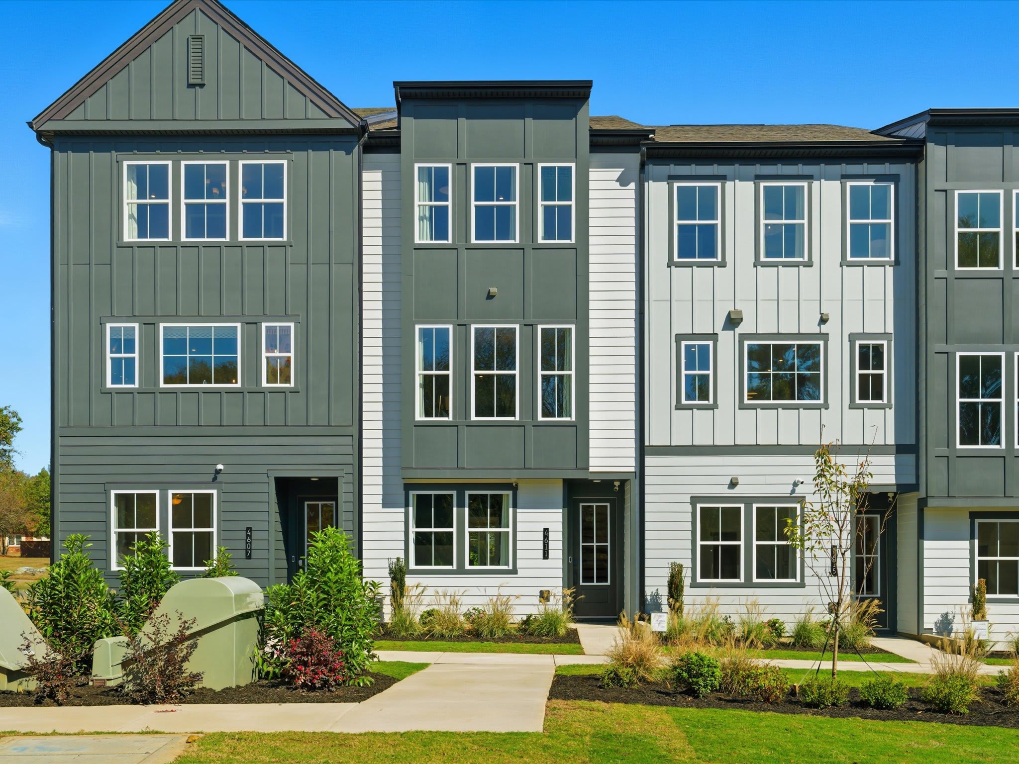 A row of modern, multi-story townhouses with green and white siding, surrounded by a well-maintained lawn and landscaping.