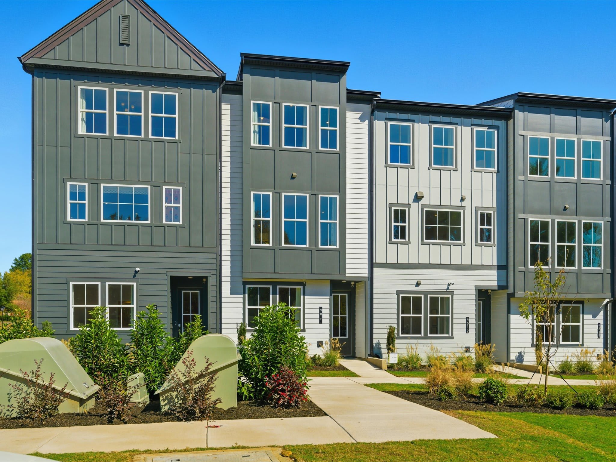 A multi-story residential building with a green exterior, surrounded by landscaped greenery and a paved walkway in the foreground.