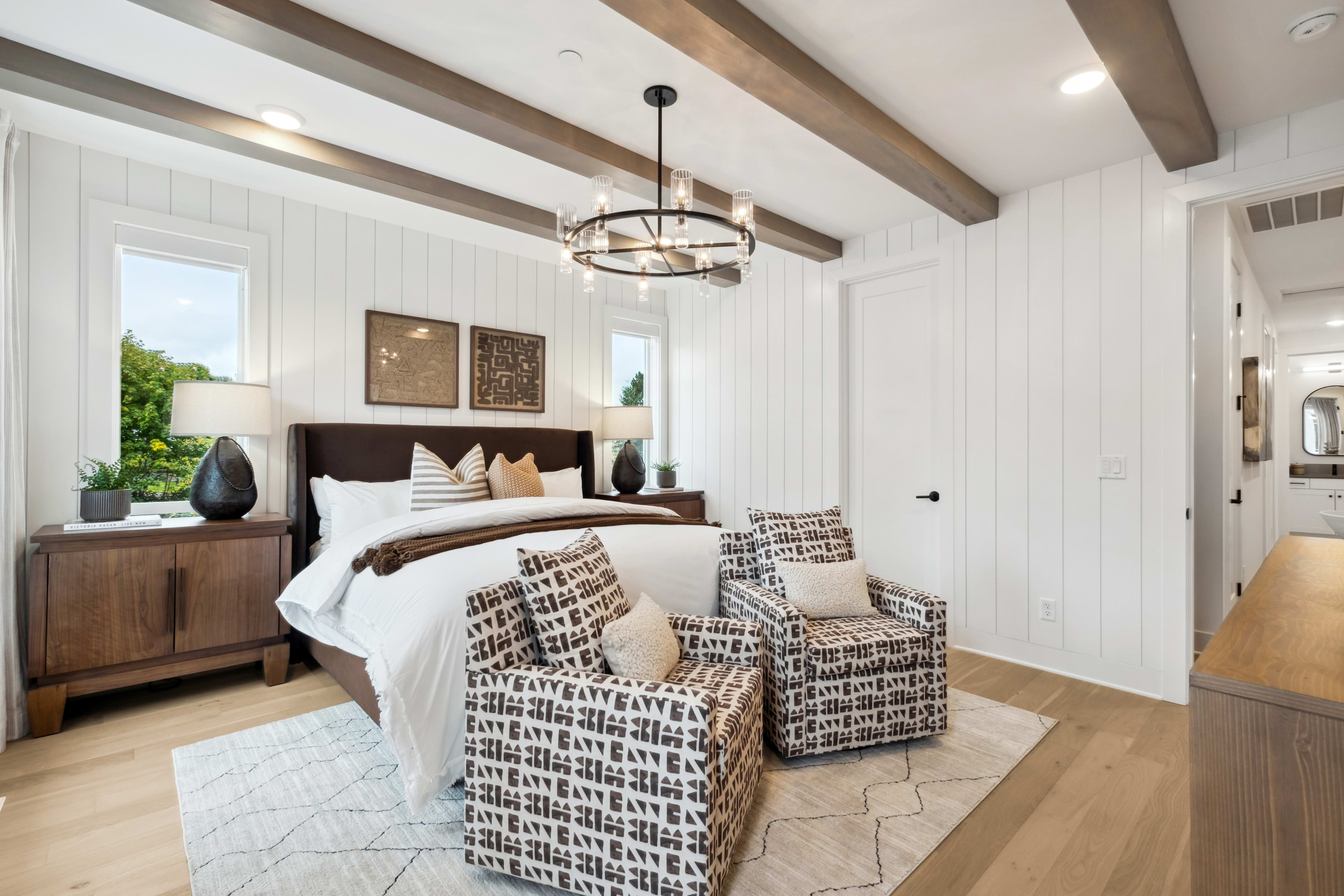 A cozy and well-appointed bedroom with a wooden ceiling, a large bed with patterned bedding, and a pair of woven chairs in the foreground.