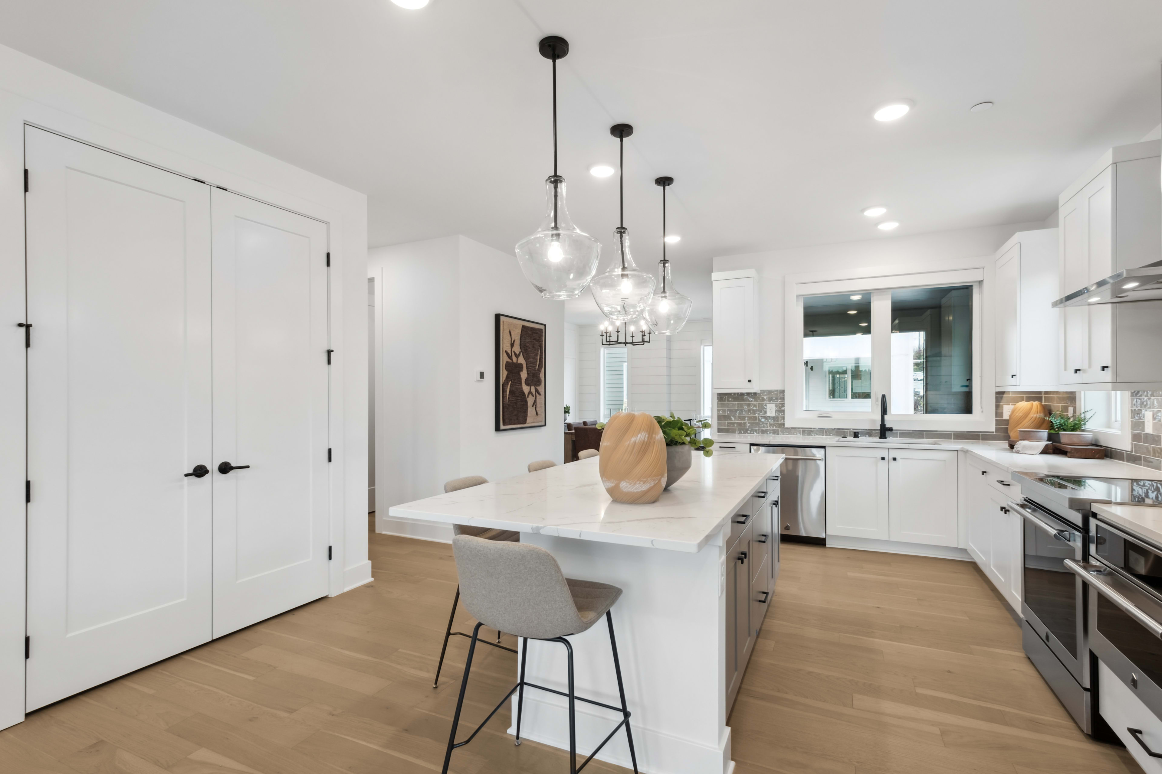 A modern, open-concept kitchen with white cabinets, a central island, and pendant lighting fixtures, set against a hardwood floor.