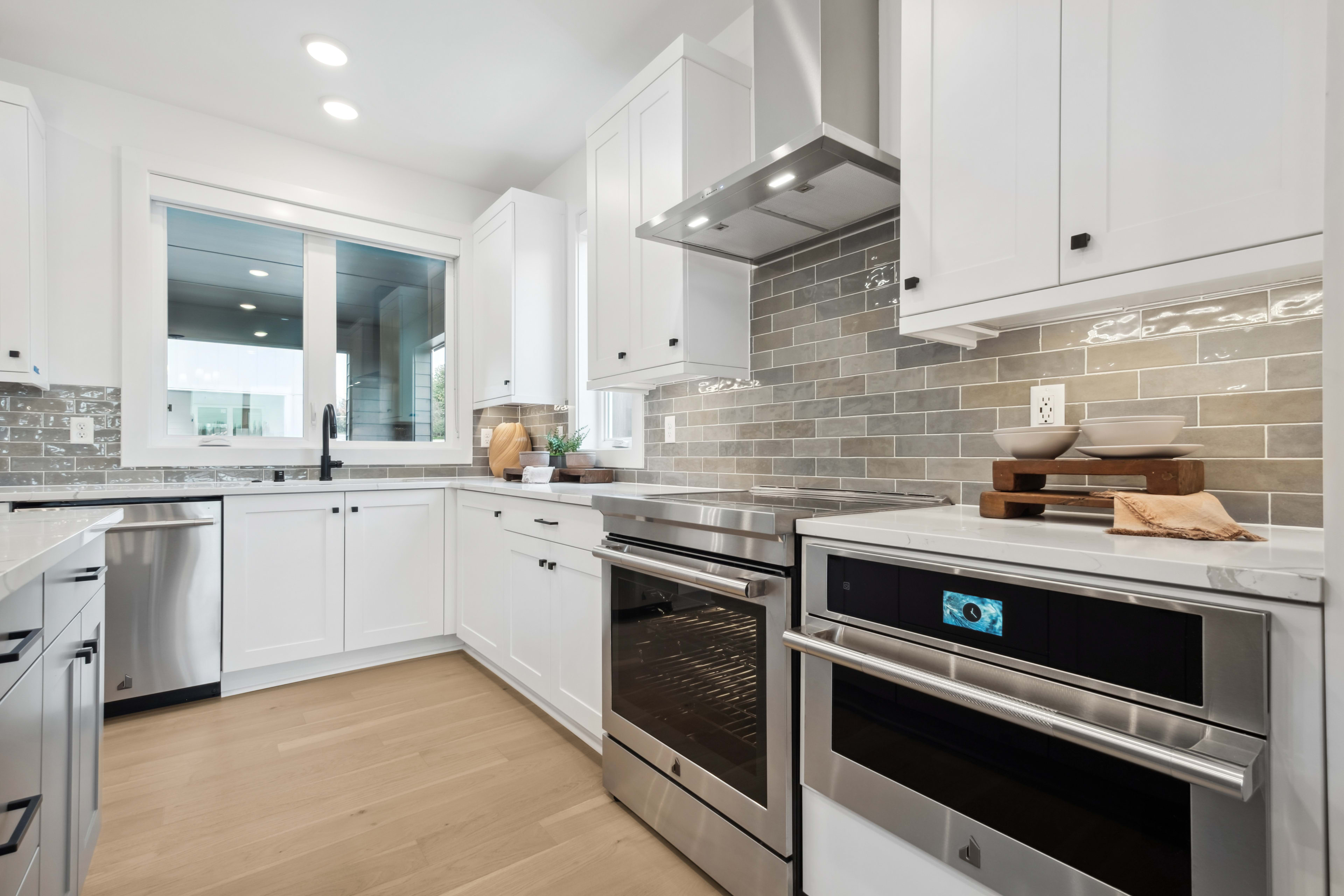 A modern, well-equipped kitchen with white cabinets, stainless steel appliances, and a tiled backsplash, set against a bright and airy background.