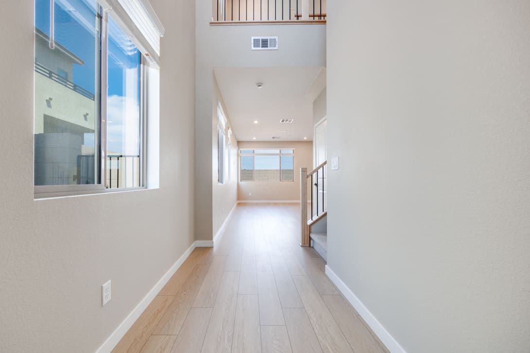 A bright, spacious hallway with white walls, wooden floors, and a large window overlooking the outdoors.