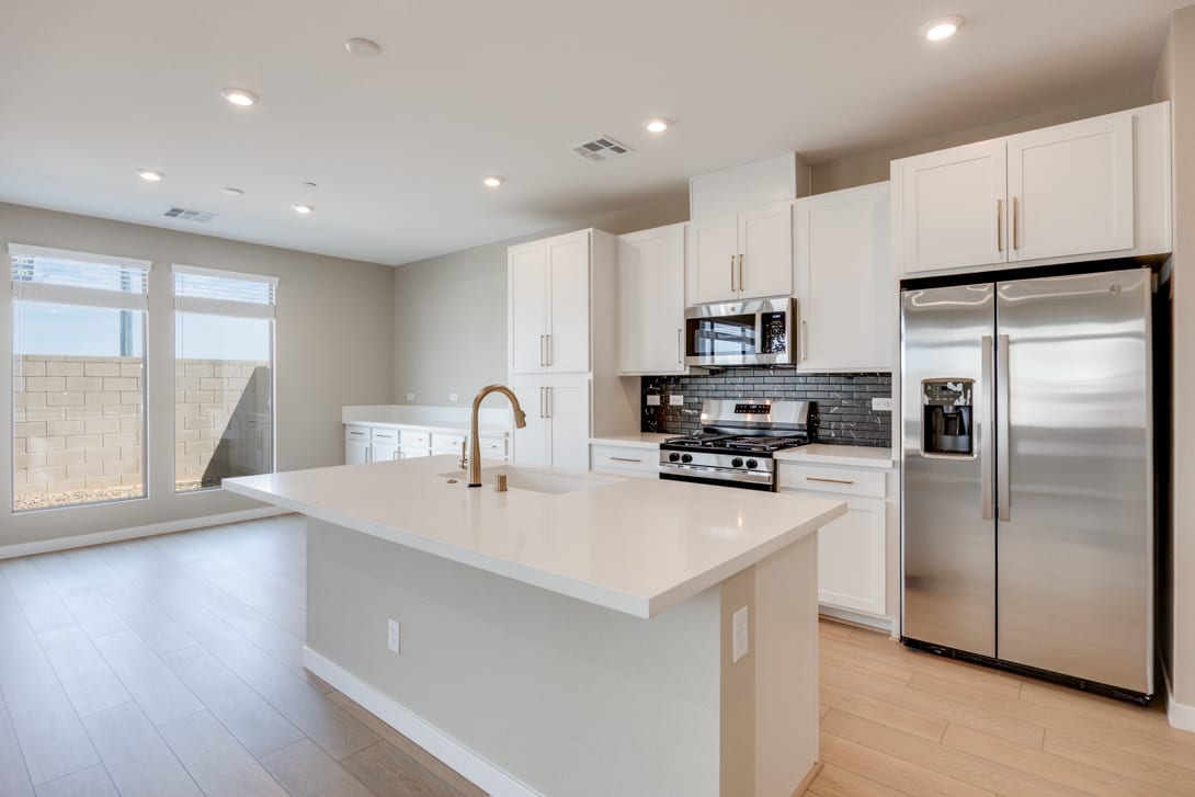 A modern, open-concept kitchen with white cabinets, stainless steel appliances, and a large island with a white countertop.