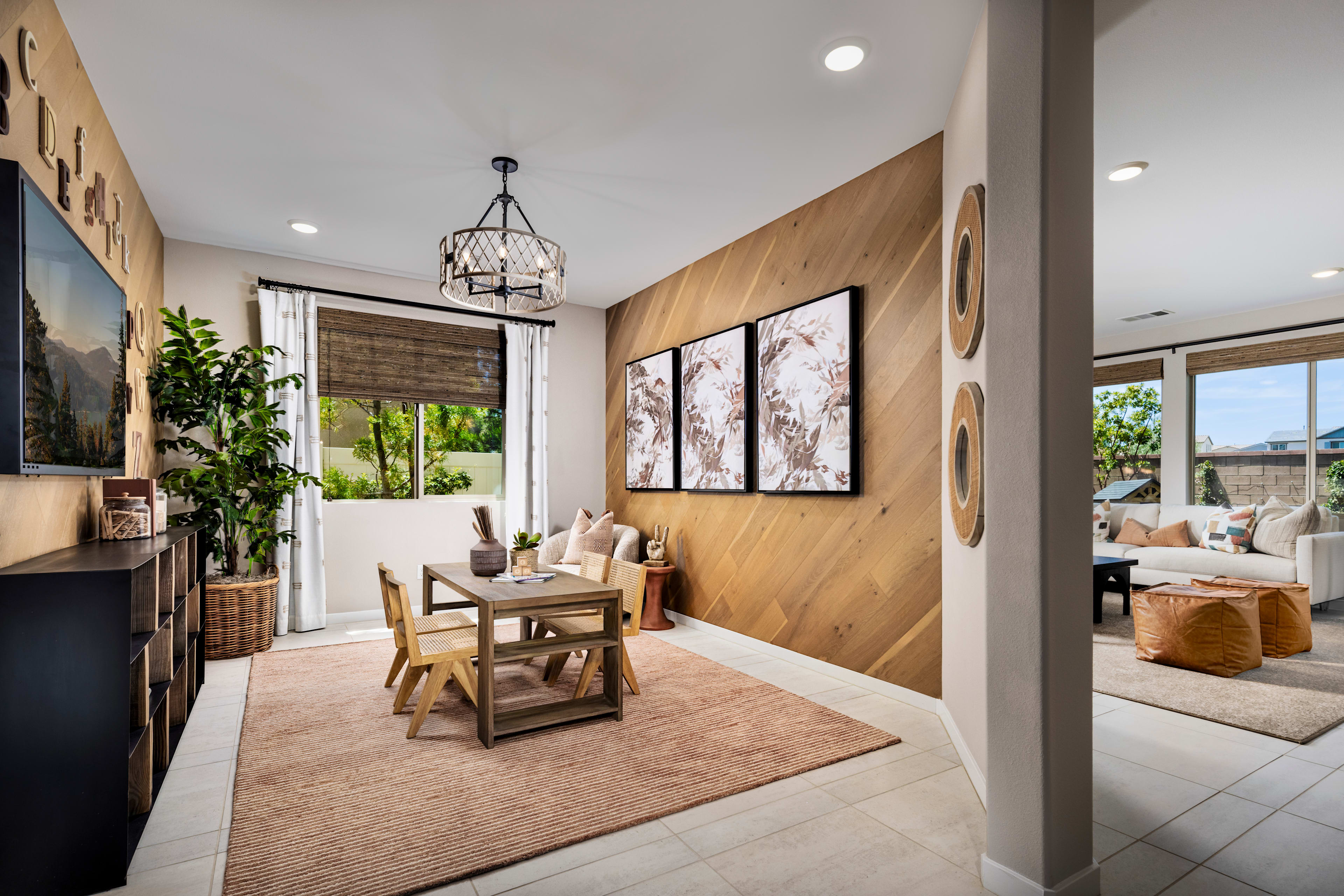 A cozy and inviting dining area with wooden paneled walls, a rustic chandelier, and a wooden table set with chairs, complemented by artwork and potted plants in the background.