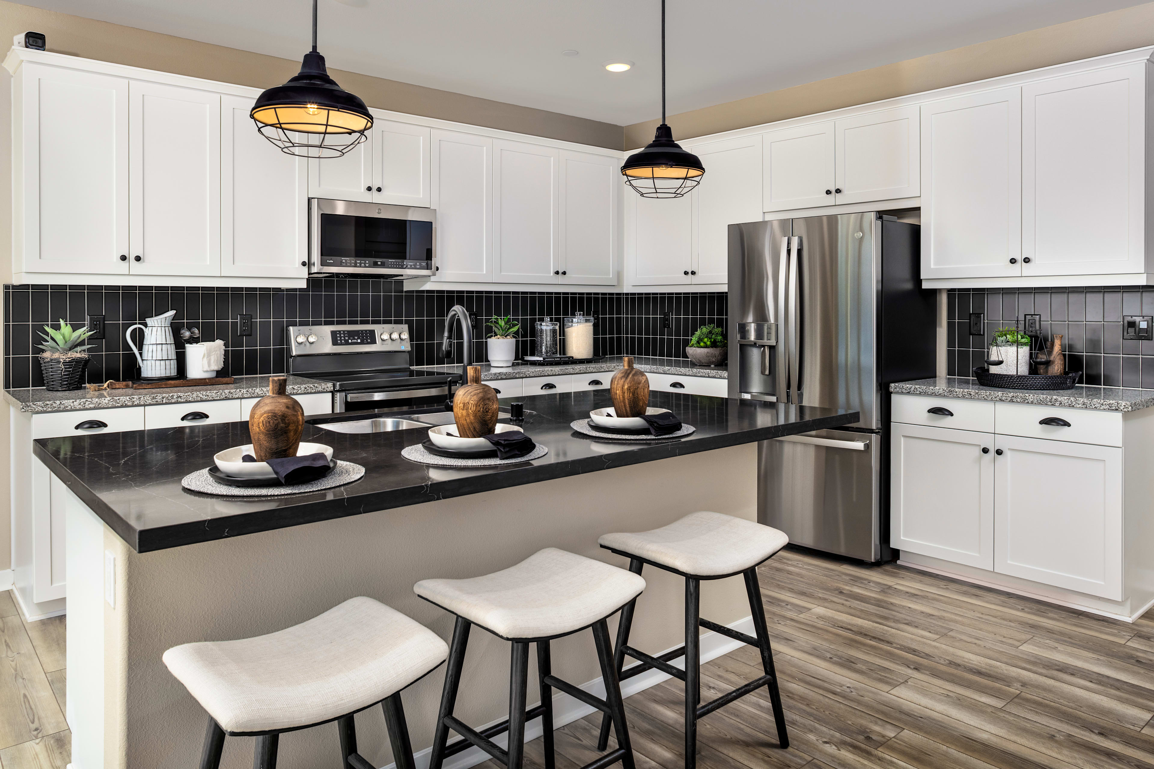 A modern and well-equipped kitchen with white cabinets, black countertops, and pendant lighting fixtures, featuring a kitchen island with stools for seating.