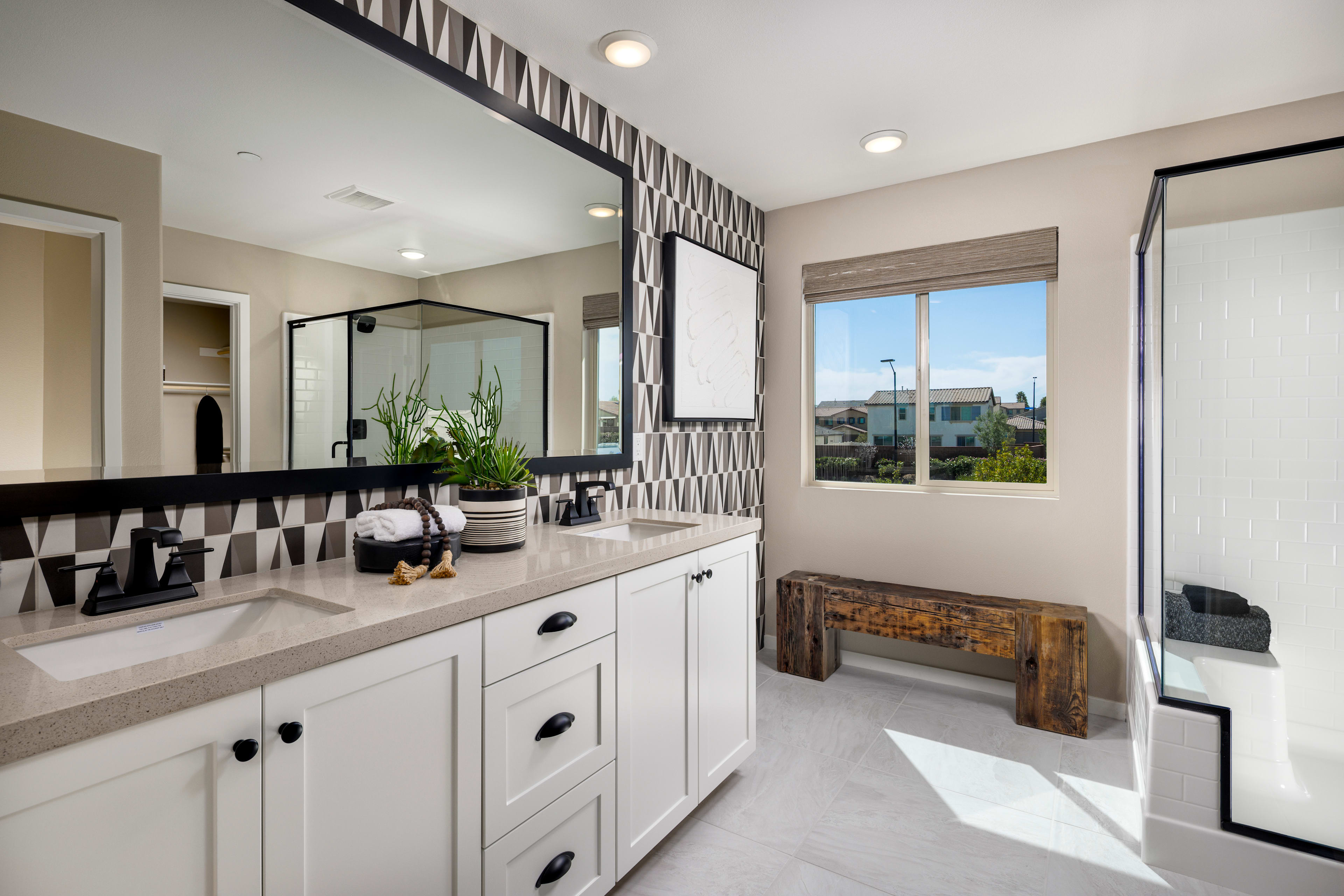 A modern and spacious bathroom with white cabinets, a large mirror, and a window overlooking an outdoor area.