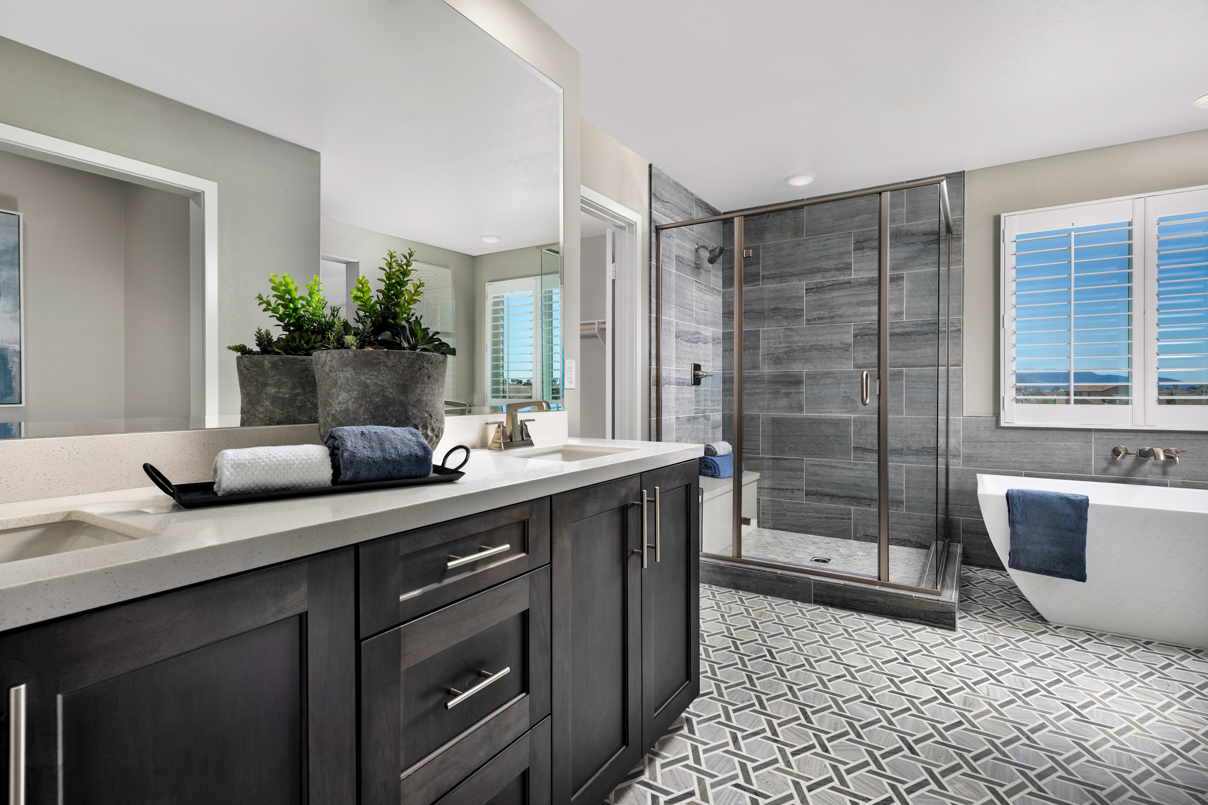 A modern and stylish bathroom with a dark vanity, a large shower enclosure, and a tiled floor featuring a geometric pattern.