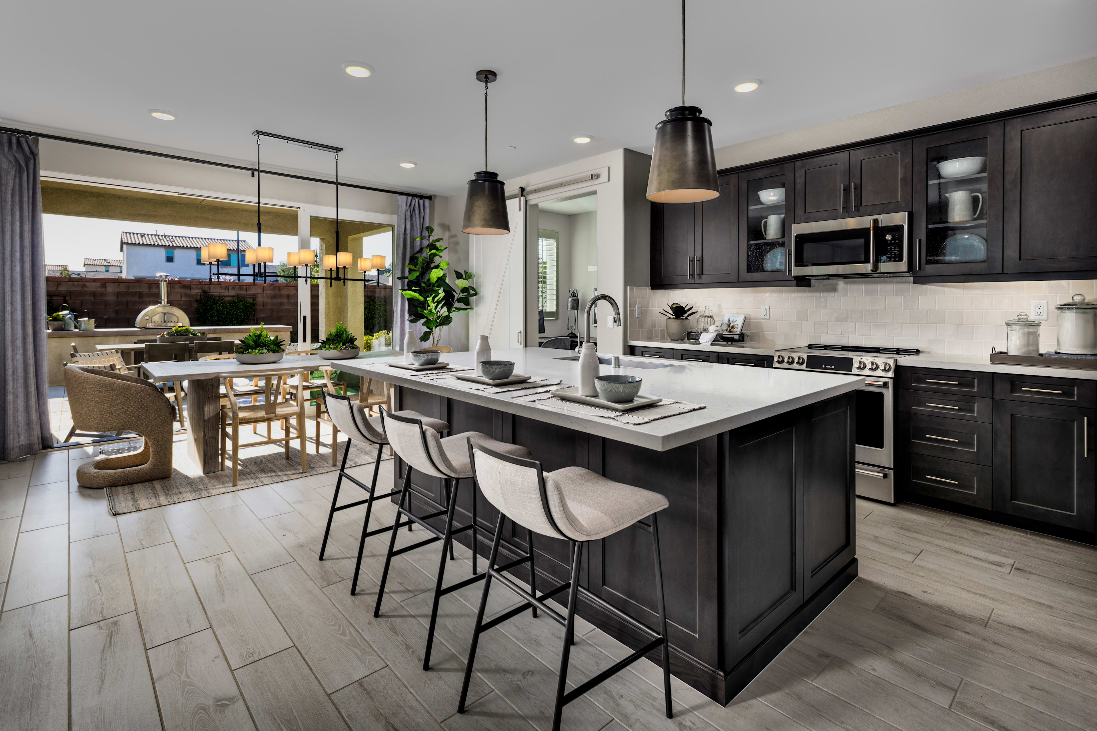 A modern and stylish kitchen with dark cabinets, a large island with bar stools, and a dining area visible in the background.