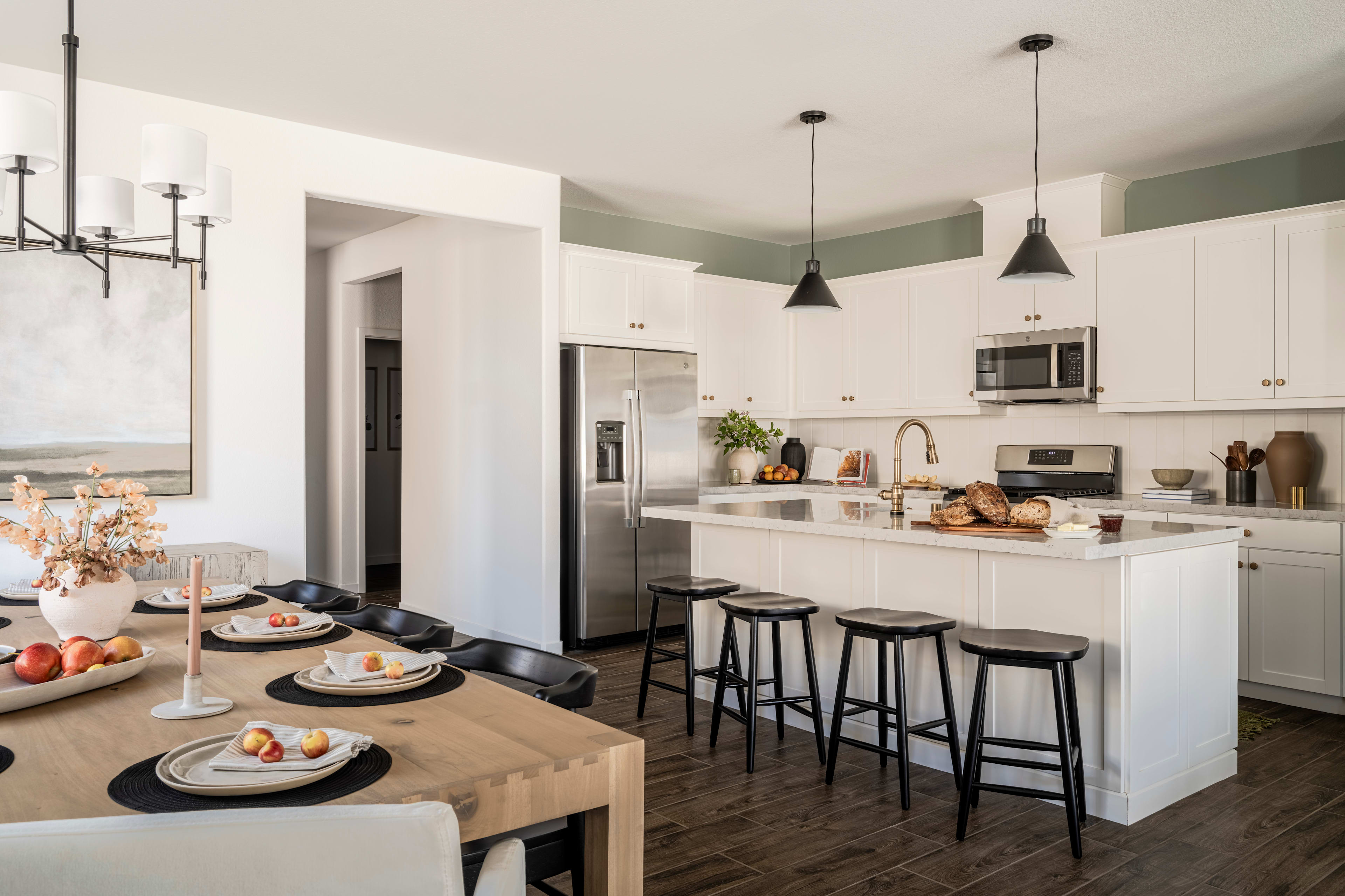 A modern, open-concept kitchen with a dining area, featuring white cabinets, wooden floors, and pendant lighting over the kitchen island.