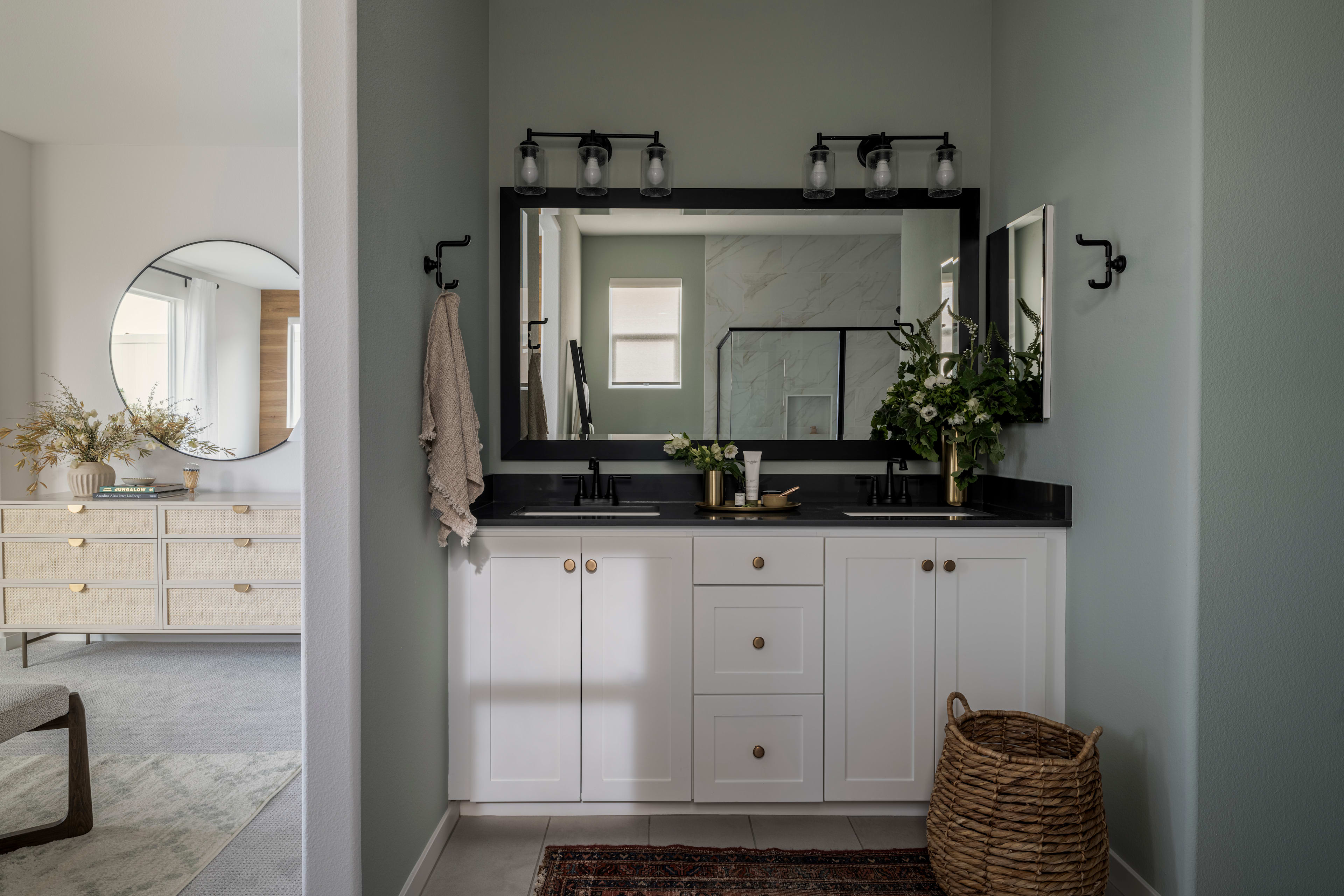 A modern and well-designed bathroom with white cabinets, a black countertop, and a large mirror with a decorative frame. A woven basket sits on the floor, adding a natural touch to the space.