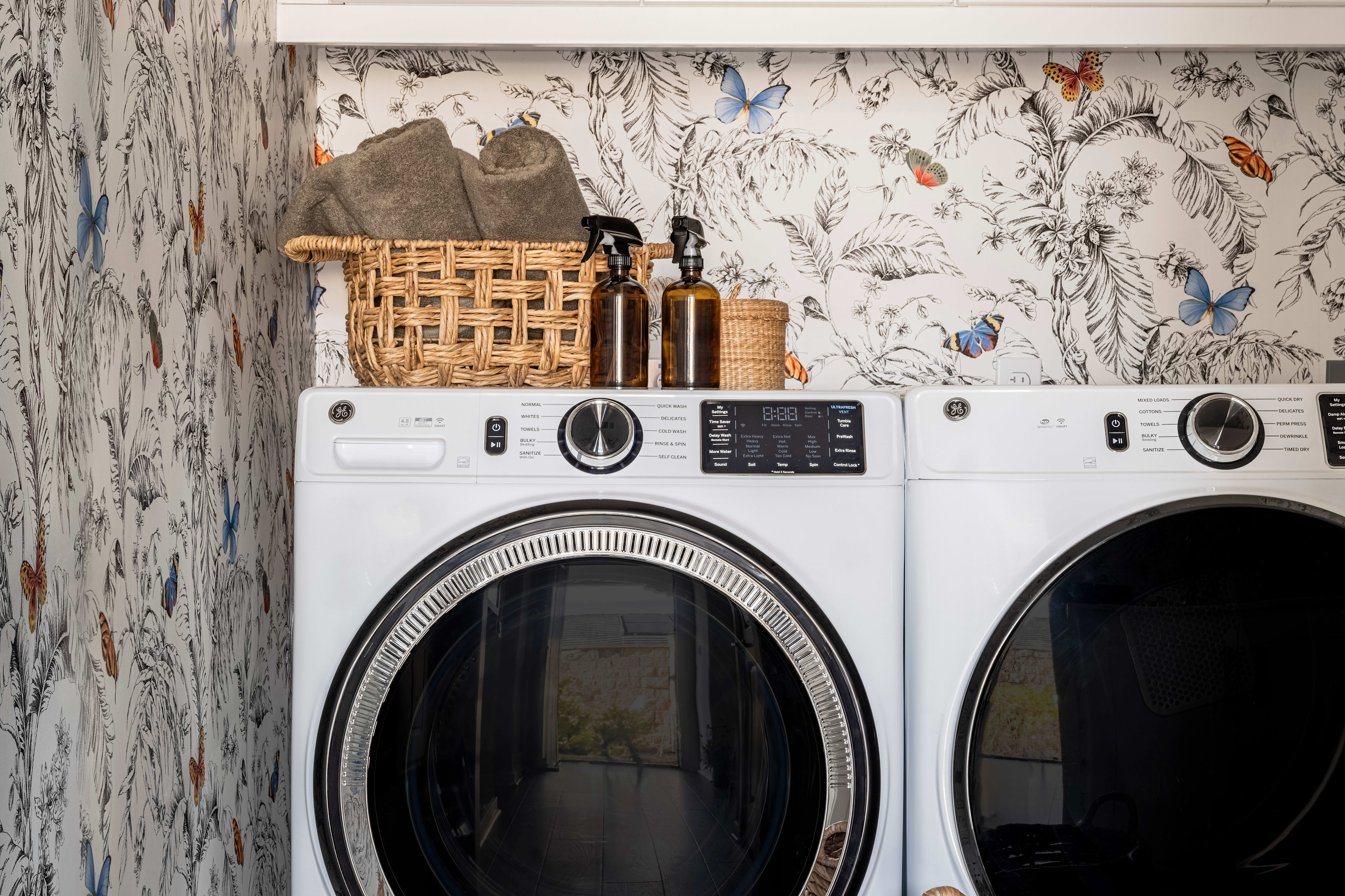 A modern laundry room with a white washer and dryer, a patterned backsplash, and wicker baskets for storage.